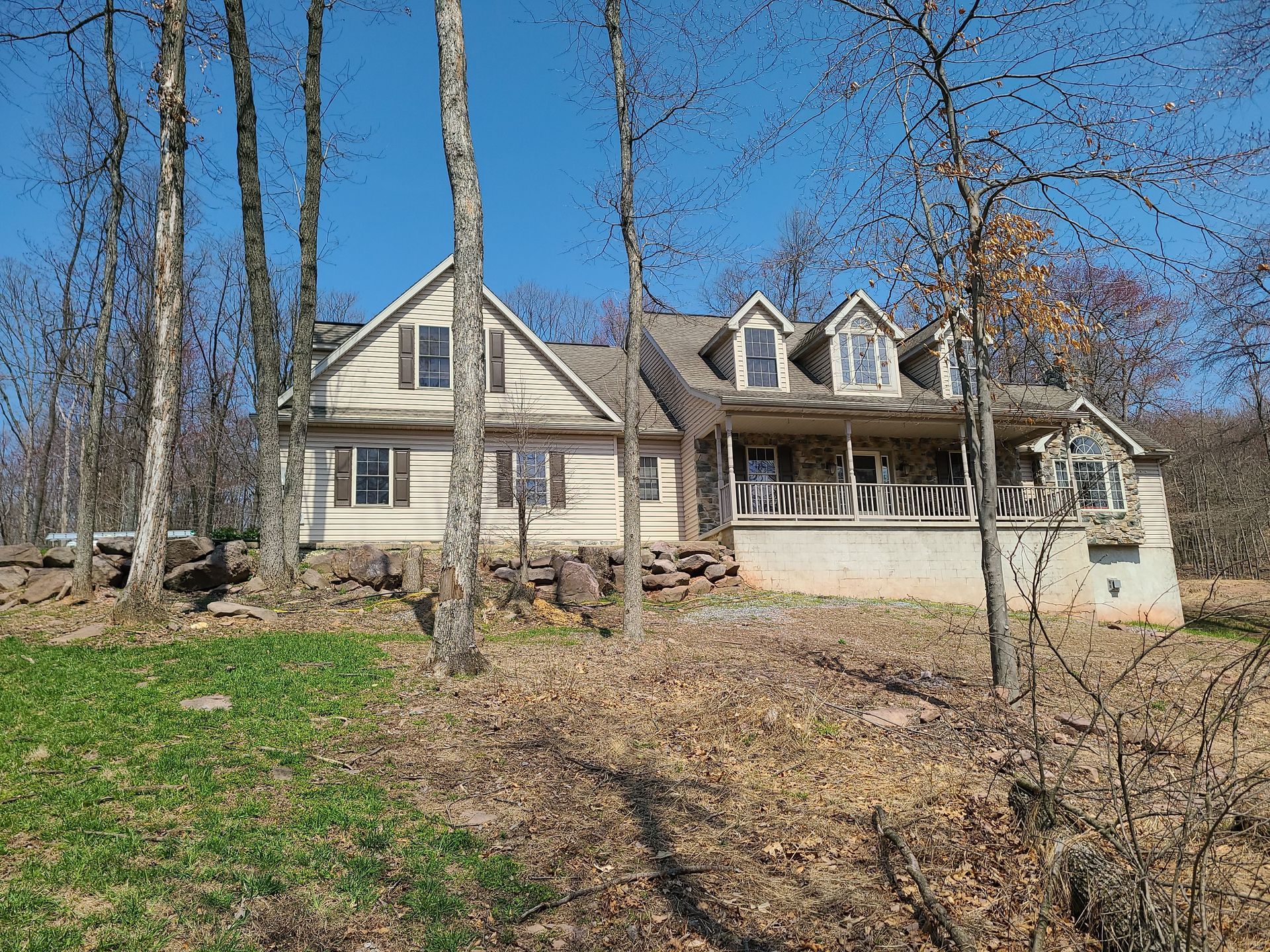 Two-story beige house with a garage, seen through leafless trees on a sunny day.