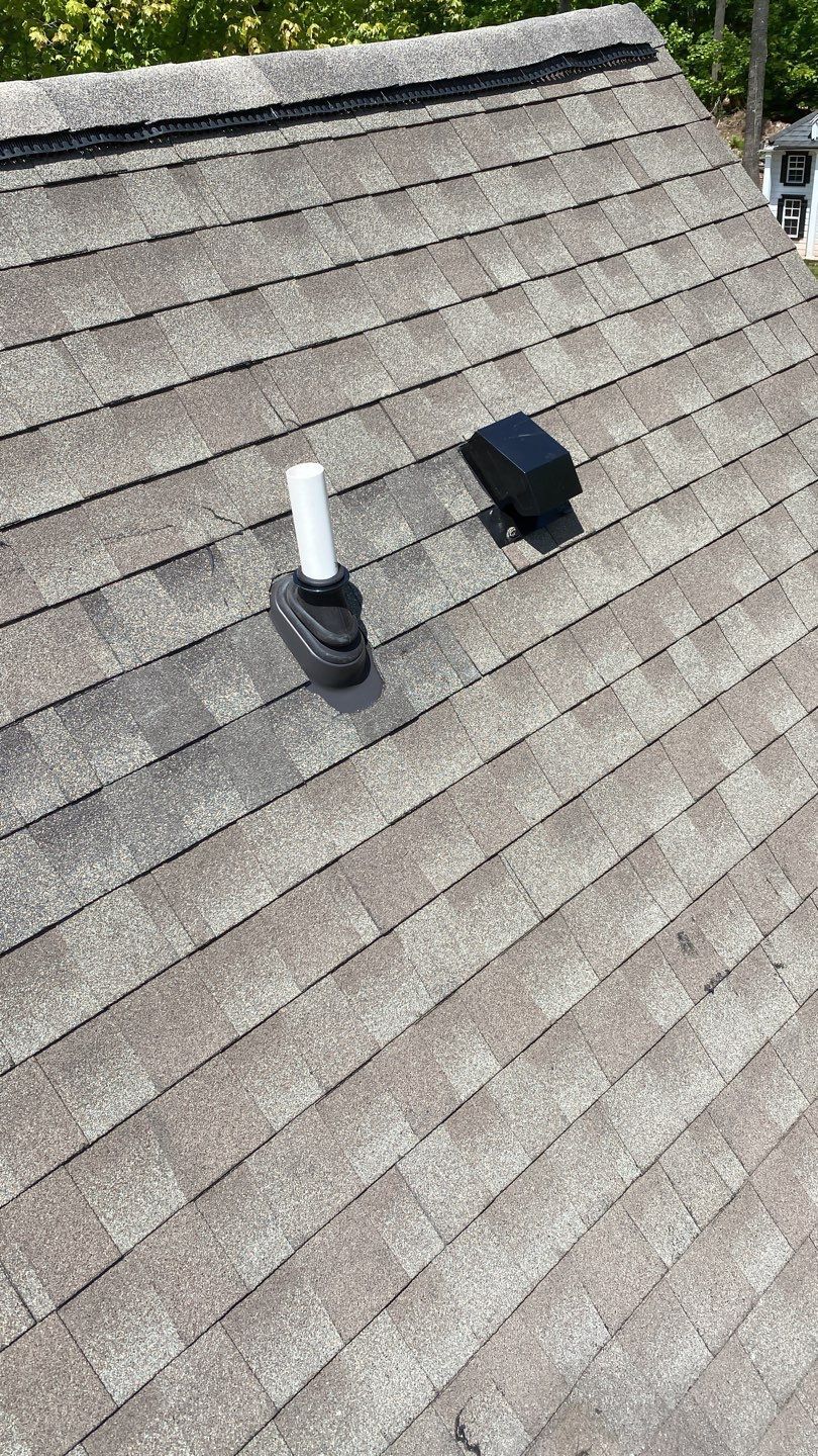 Gray shingled roof with two black rooftop vents, one topped by a white pipe.