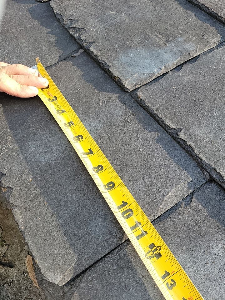 Close-up of cracked and weathered slate roofing tiles being measured during a roof inspection on North Church Street in Quarryville, PA.