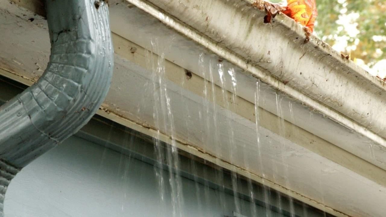 Water leaking from a gutter down the side of a house, dripping along the roof edge.
