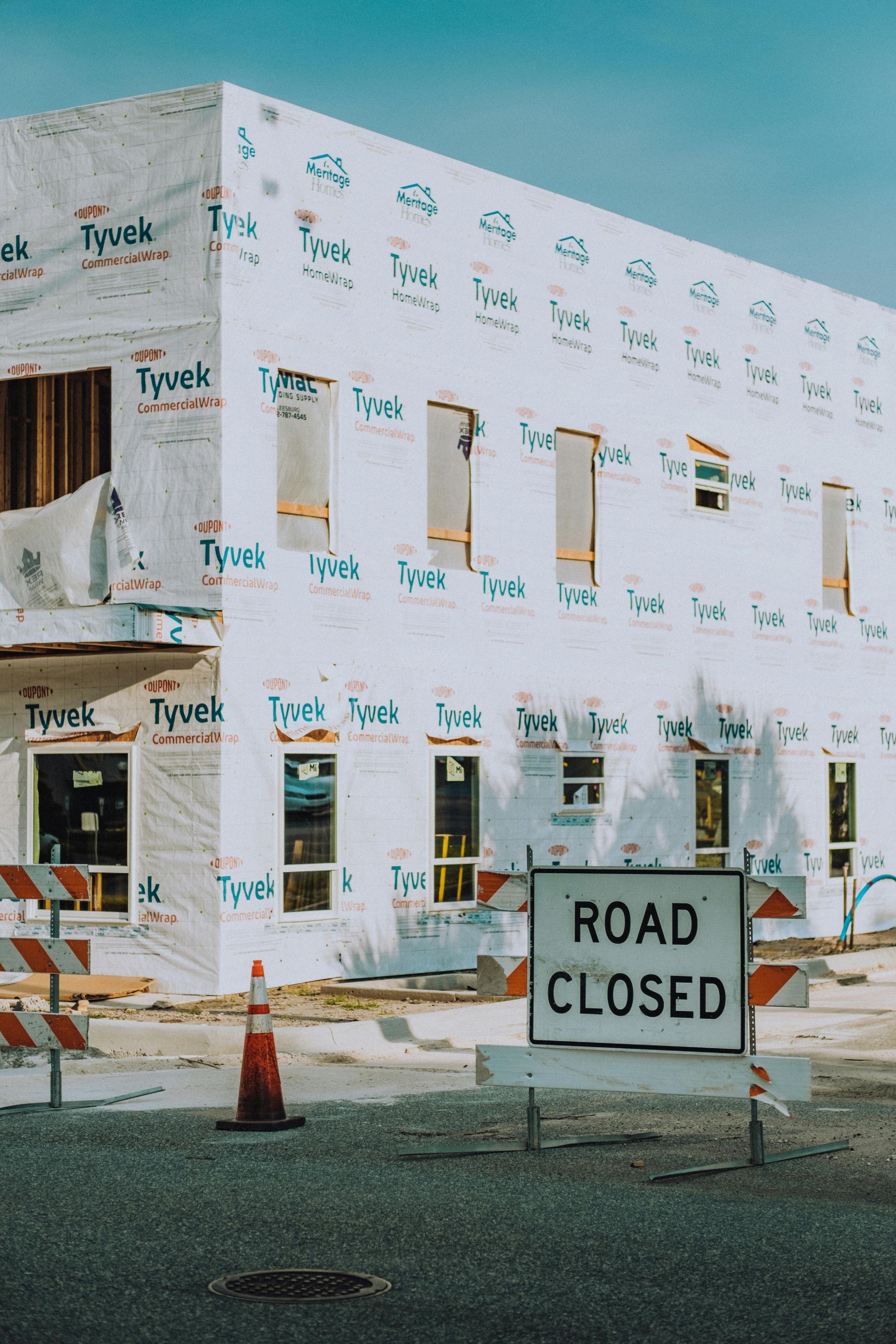 Partially built house wrapped in Tyvek with a road closed sign and traffic cones in front