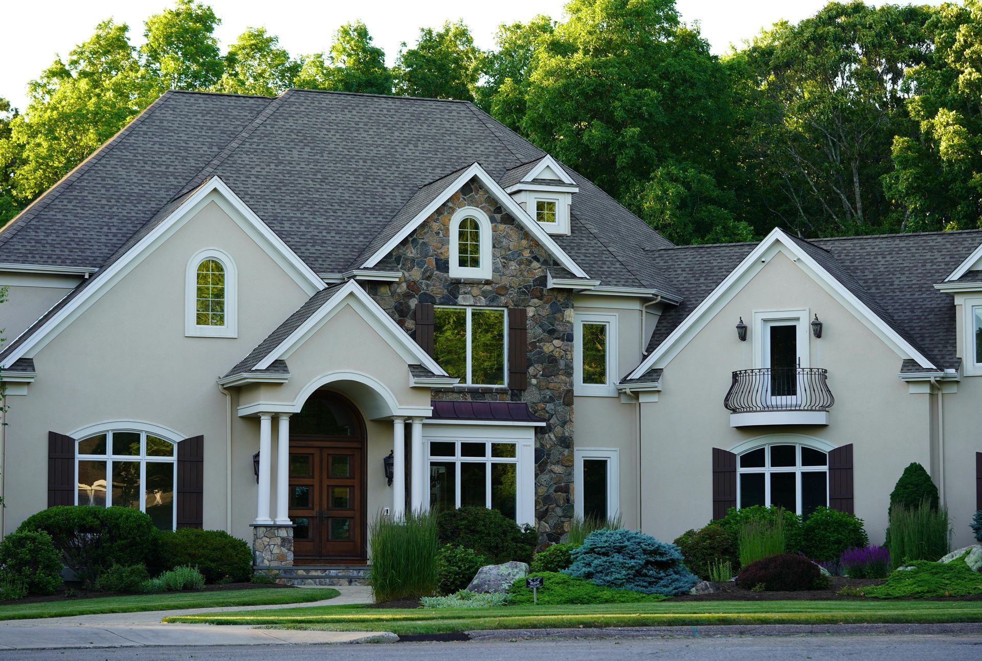 Stone house with partial cedar shake roof on a sunny day. Green lawn and trees in the front yard.