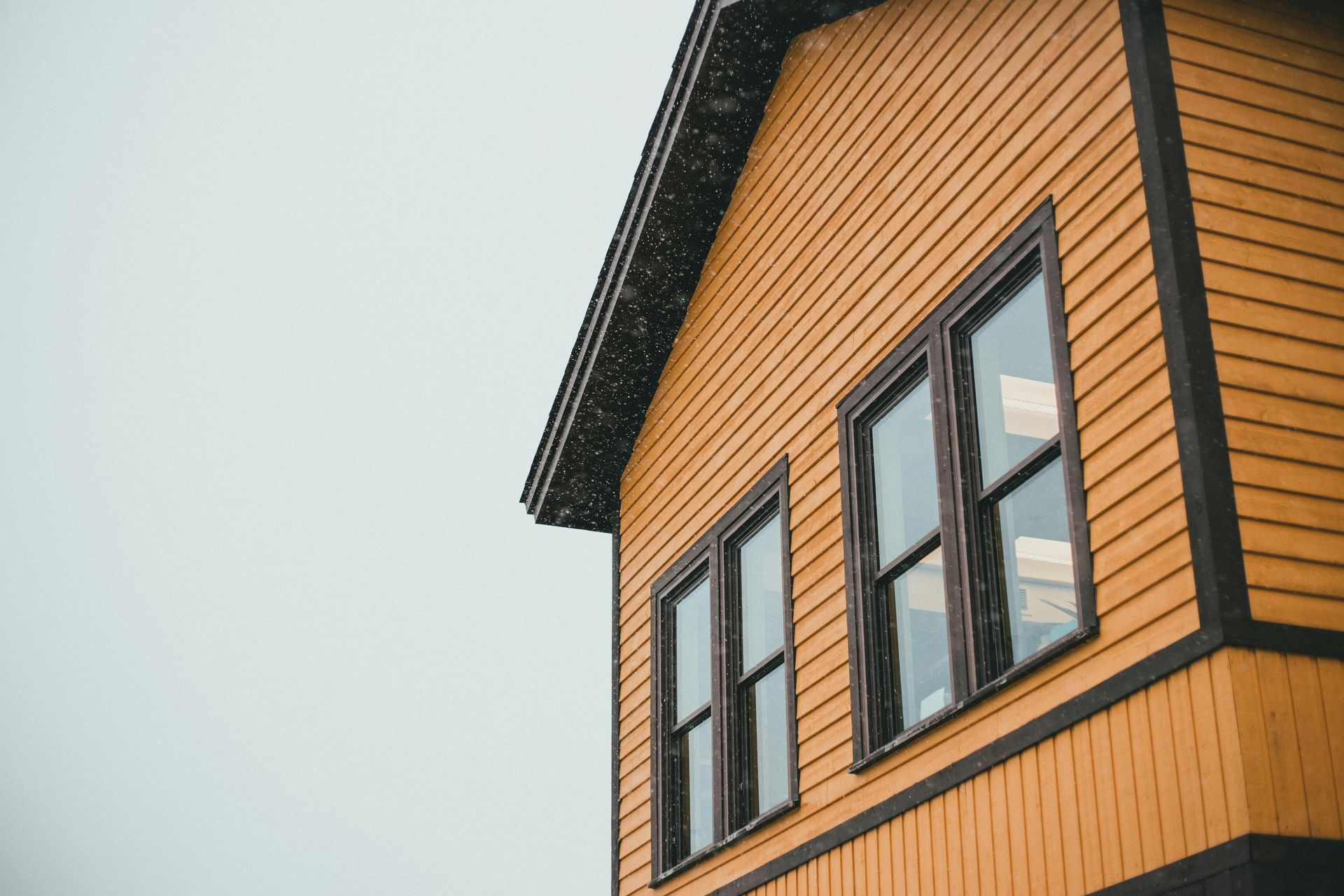 House siding partially removed, revealing plywood. A-frame roofline with ladder.