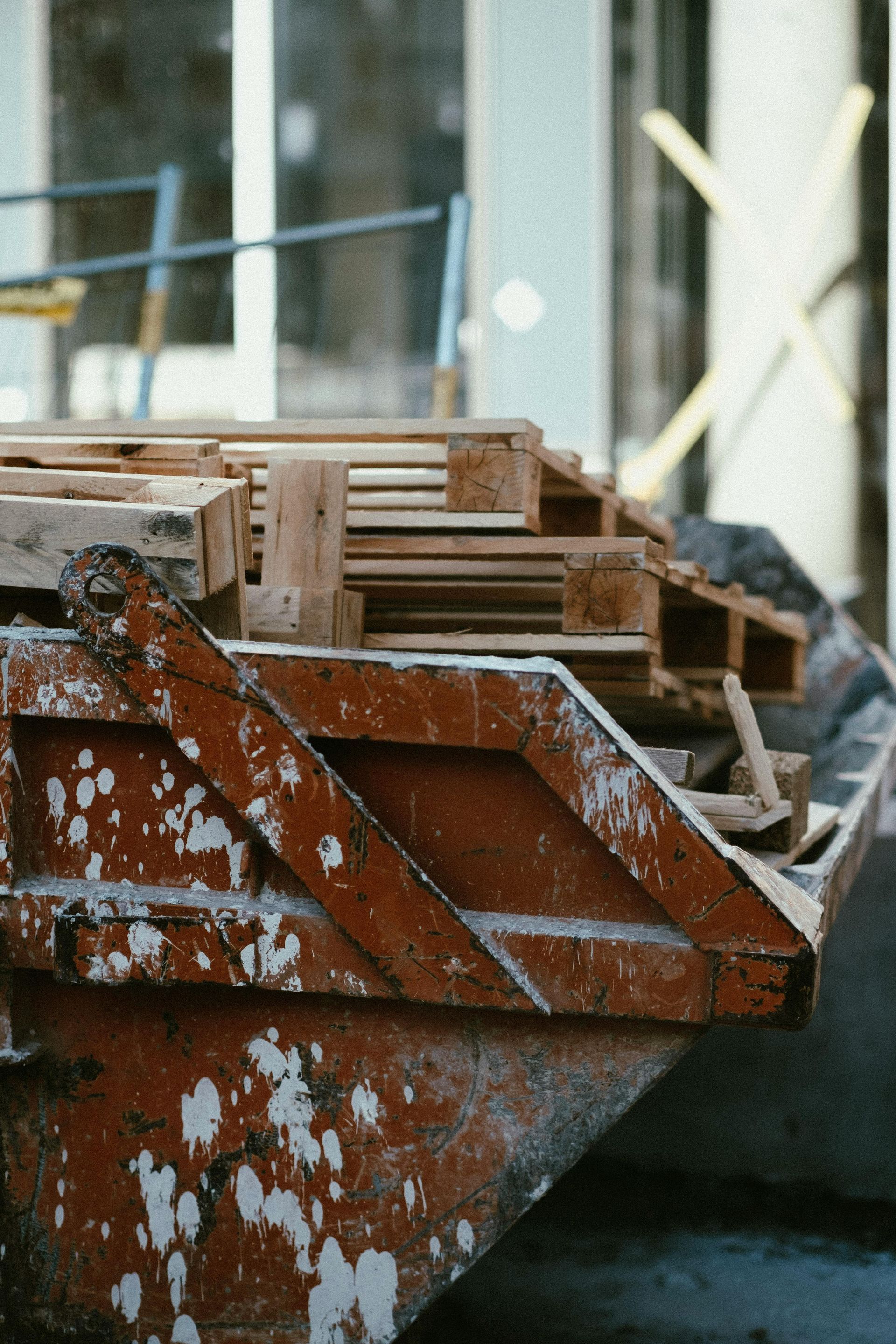 Red dumpster filled with wooden pallets at a construction site.
