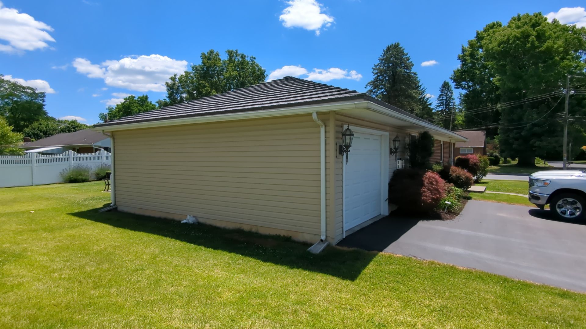 Beige single-story garage with a dark roof beside a driveway and green lawn on a sunny day