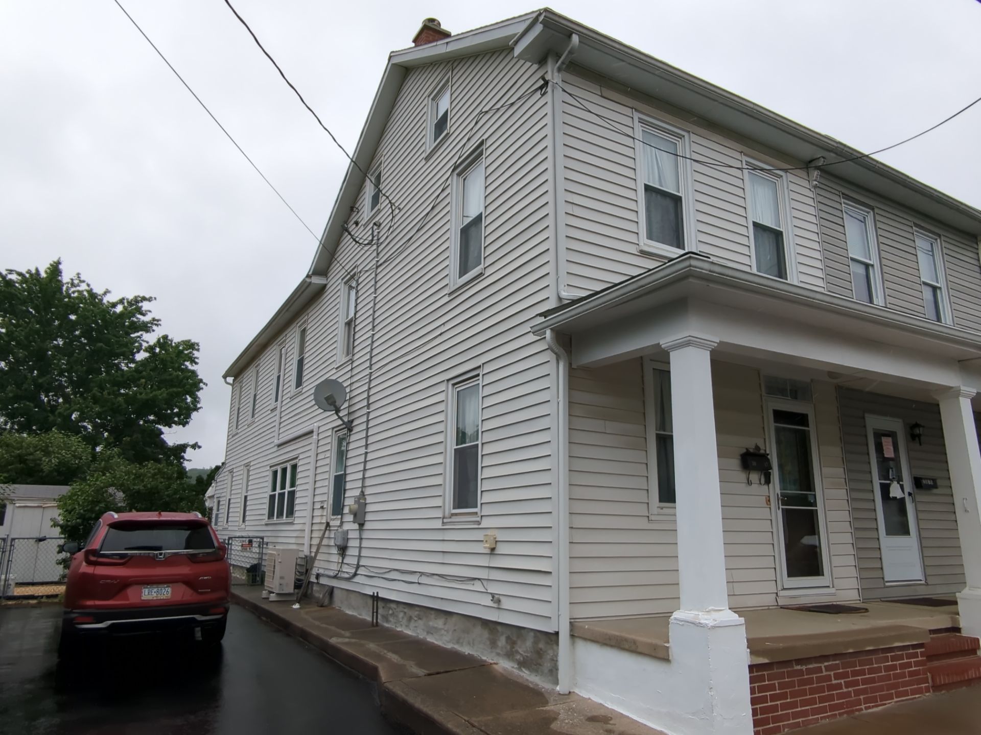 White two-story house with porch and red SUV parked beside it on a cloudy day