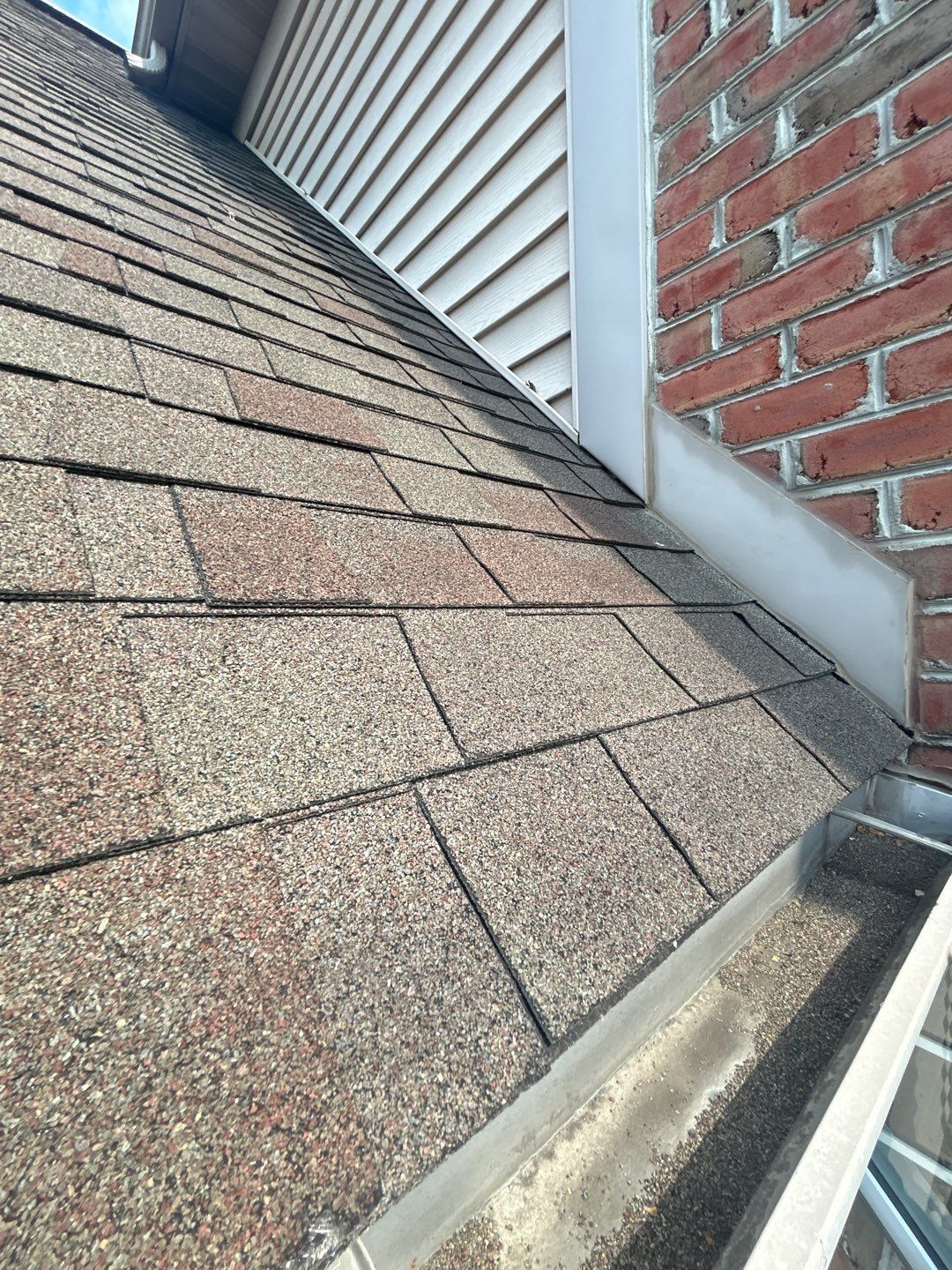 Shingled roof meeting white siding and red brick wall with a gutter along the edge