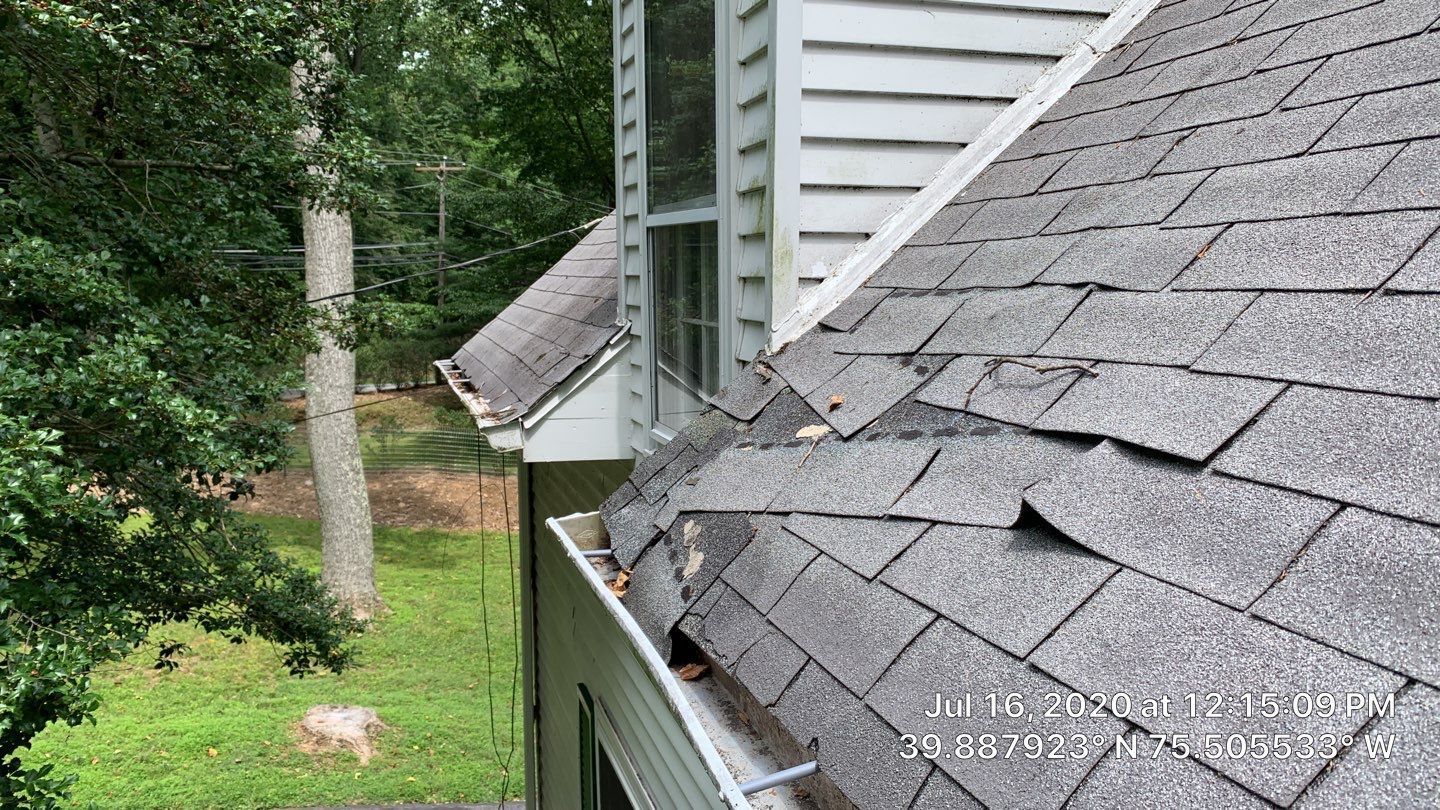 Damaged asphalt shingles and gutter along a residential roof on Cheyney Road in Glen Mills PA