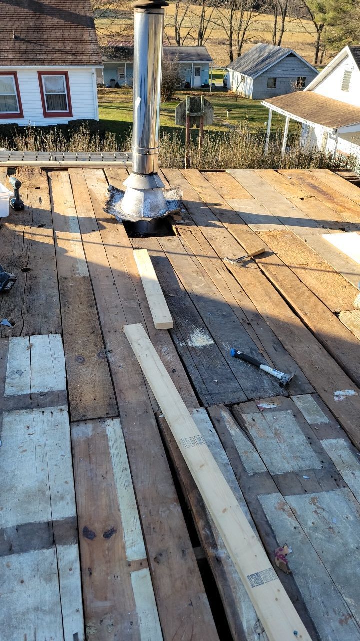 Flat rooftop with a metal chimney vent and scattered wooden planks under construction.