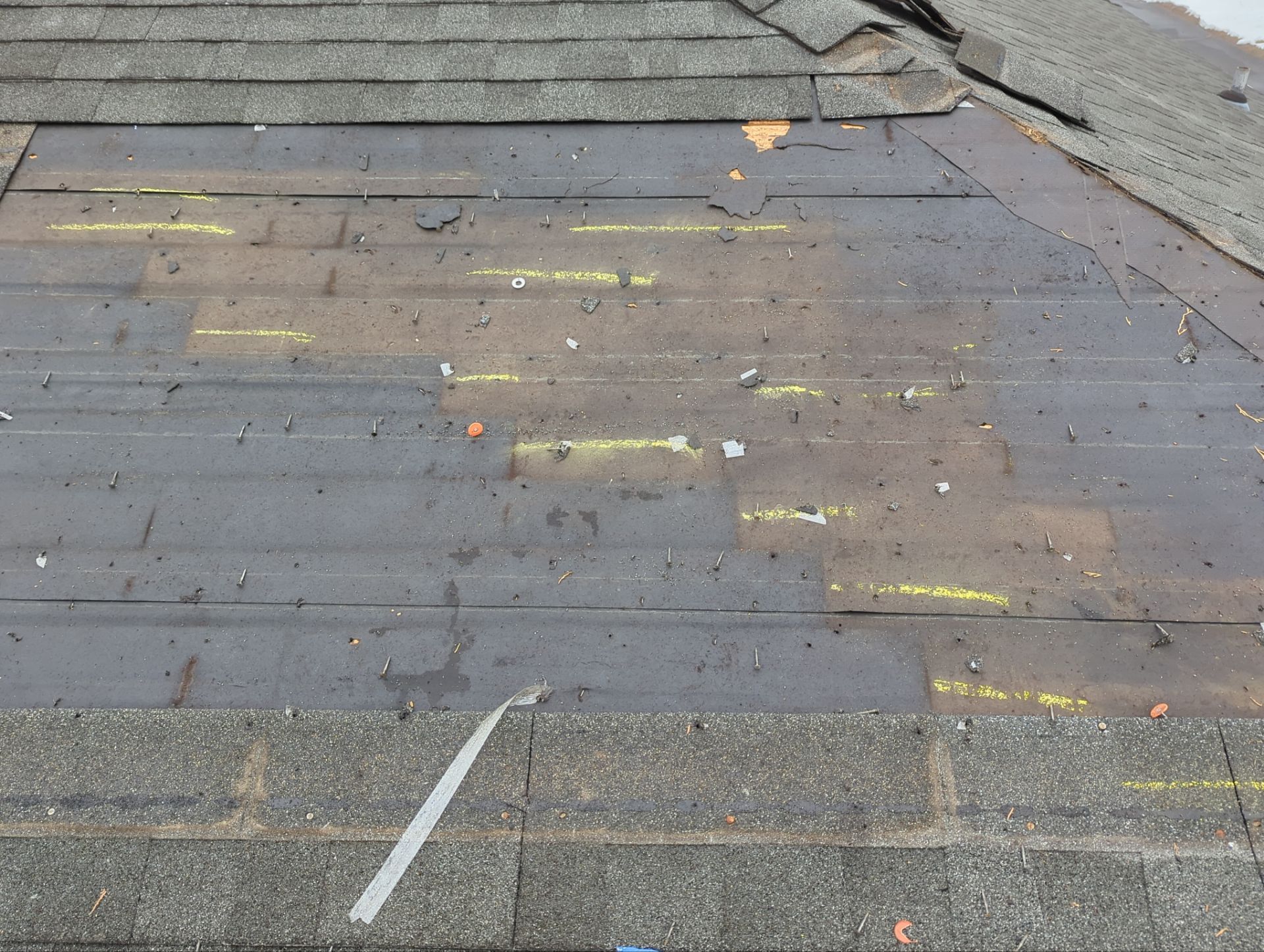 Damaged roof shingles with peeling patches and debris near the edge of a roof