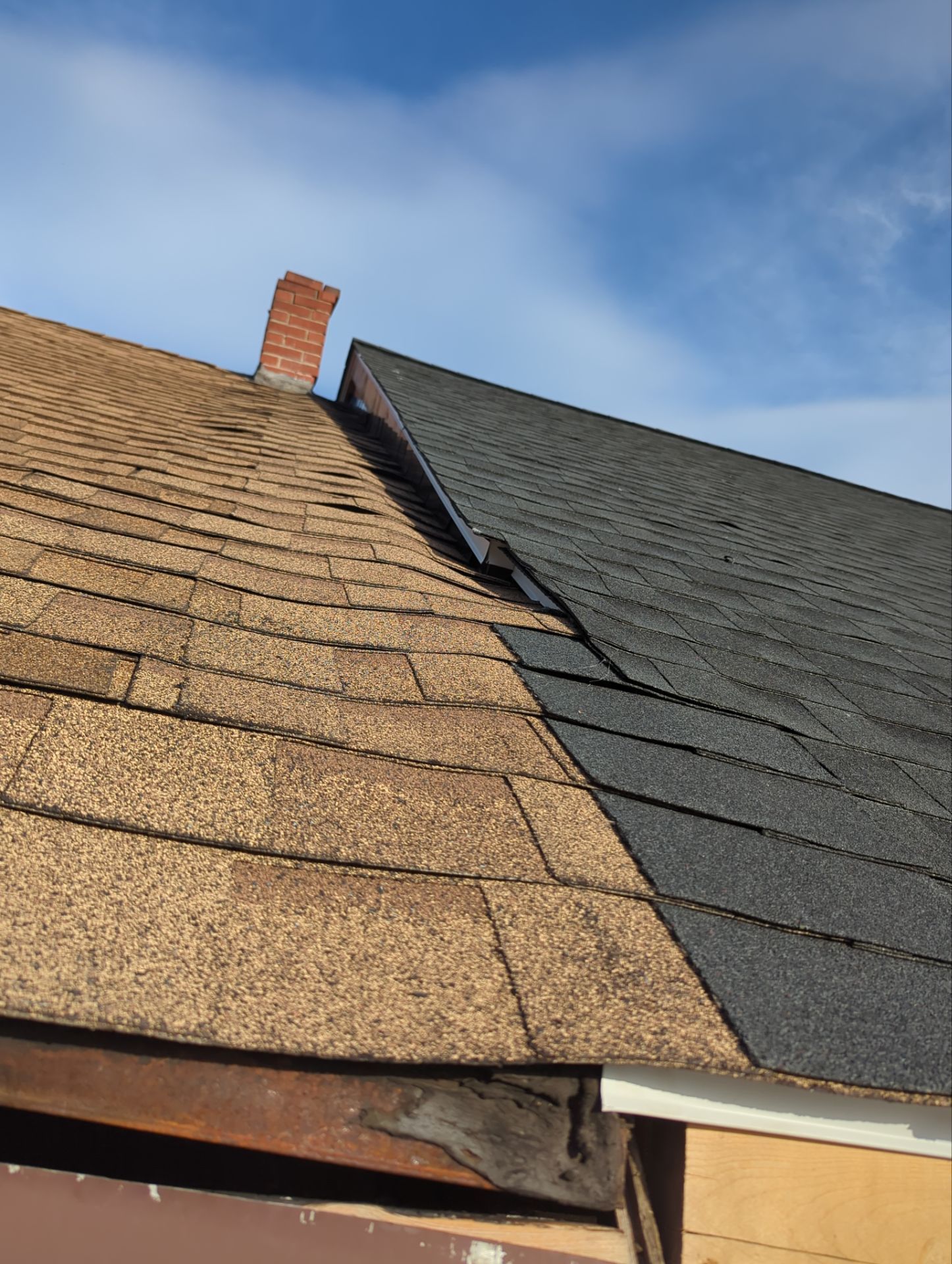 Close-up of a roof with brown and gray shingles and a brick chimney against a blue sky