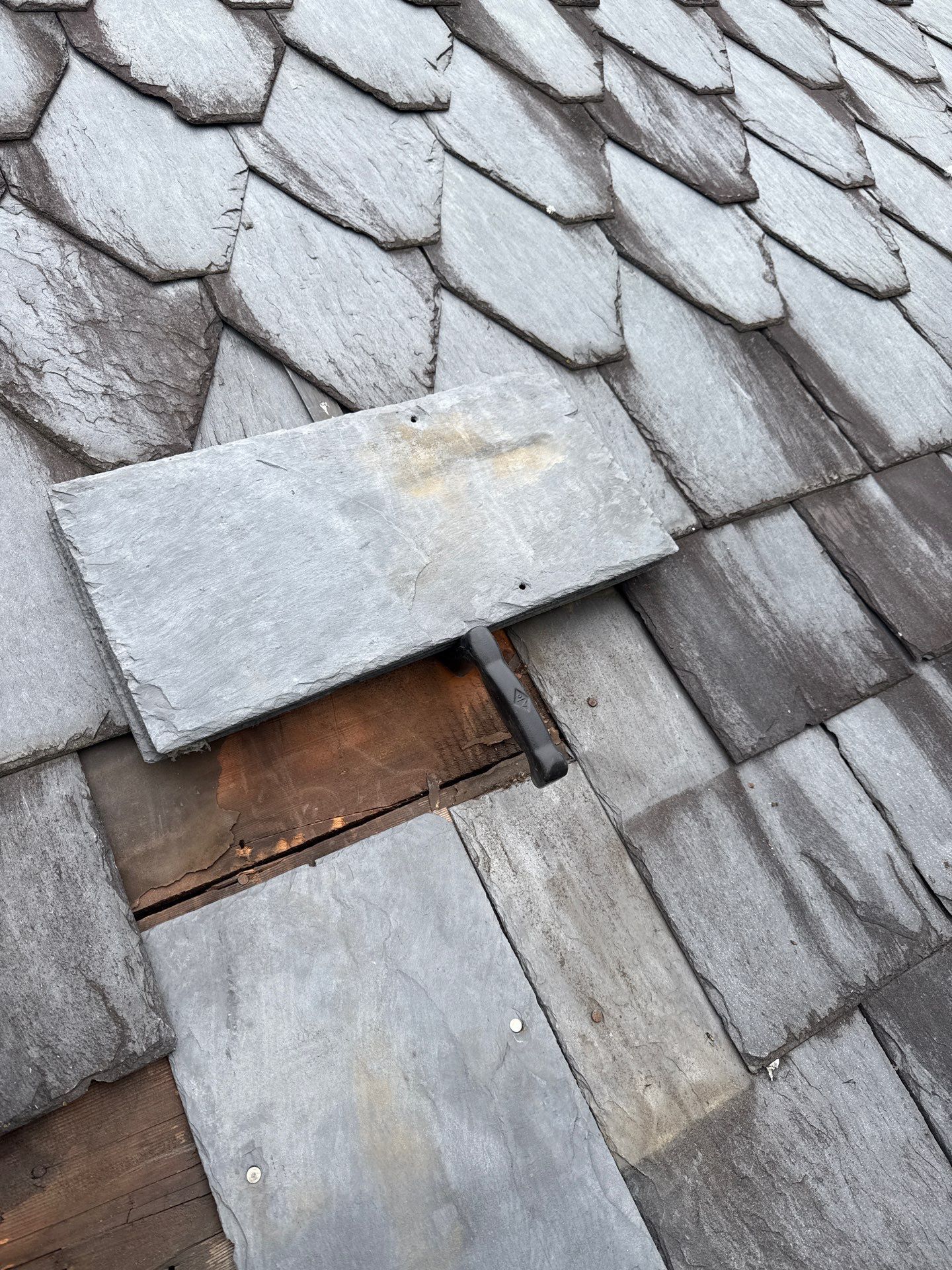 Damaged slate roof undergoing repair on Coal Hill Road in Stewartstown, PA, with broken slate tiles removed to access the roof decking for repairs.