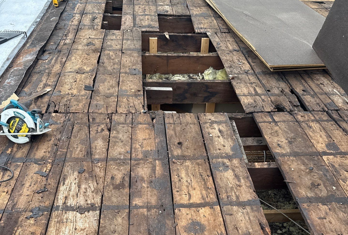 Water-damaged wooden roof decking with several large gaps and missing boards