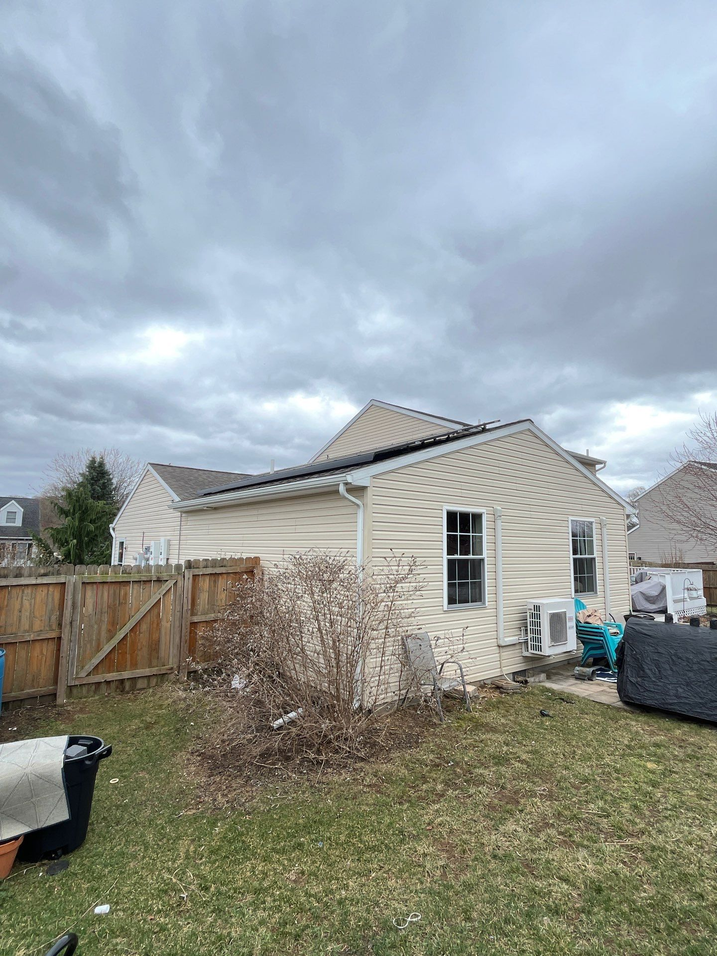 Backyard with a beige house, wooden fence, and cloudy sky after a storm