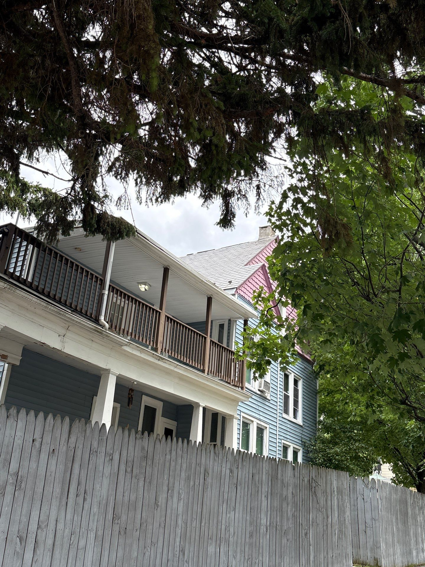 Residential houses viewed through trees behind a tall white fence