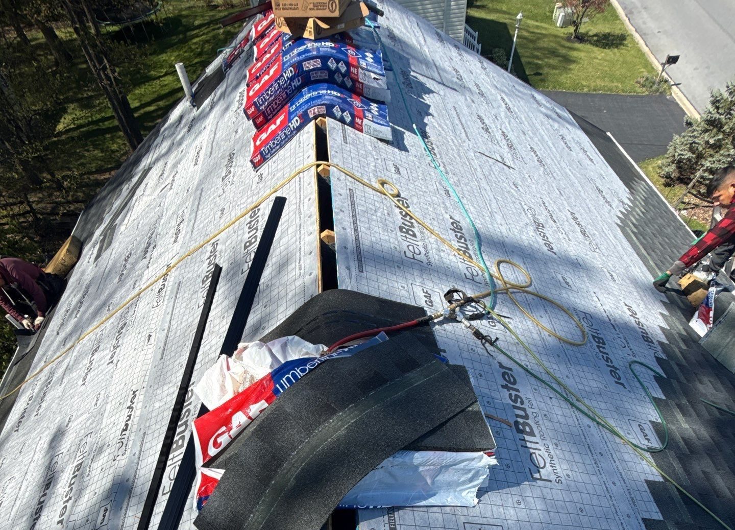 Workers repairing a steep roof with roofing materials and safety ropes