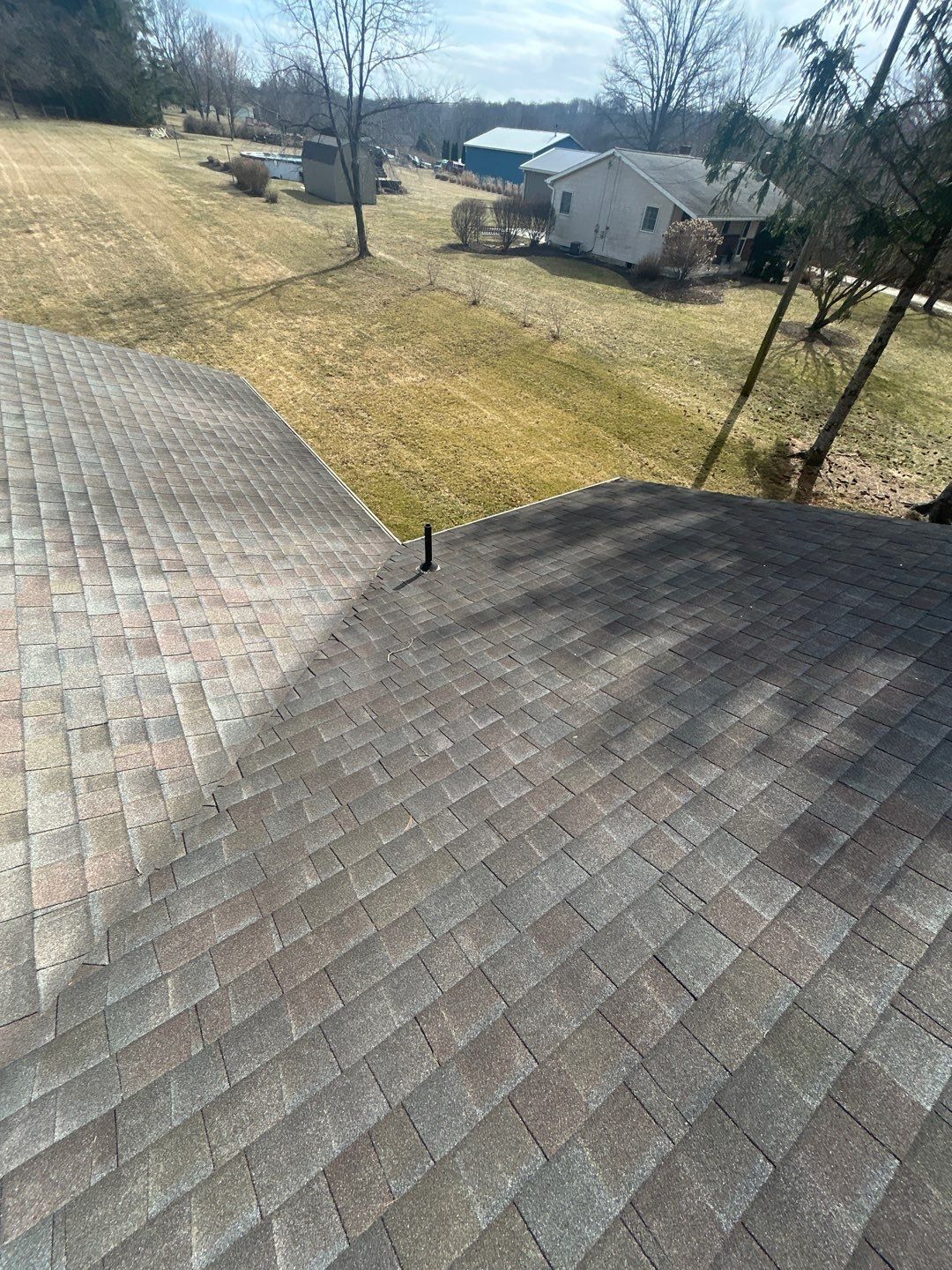 Roof shingles viewed from above, with a grassy yard and house in the background.