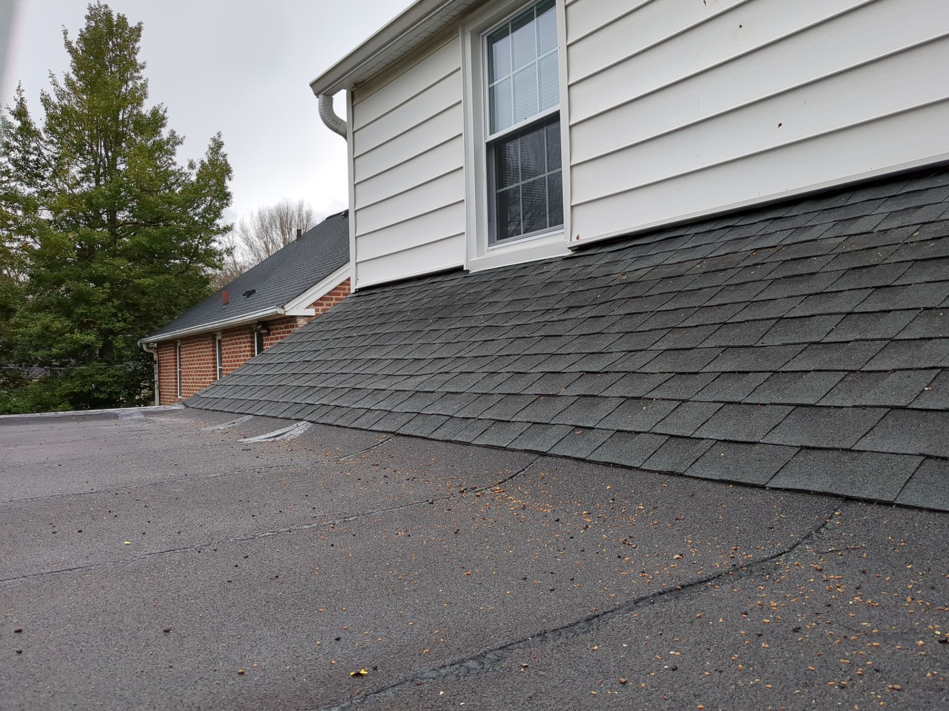 Rooftop with flat black roofing, white vents, and a damaged red-brick wall beside trees and nearby houses