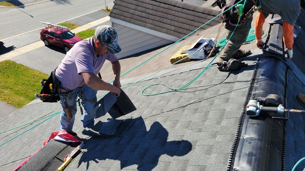 Workers installing roofing on a steep roof, securing materials with ropes and tools.