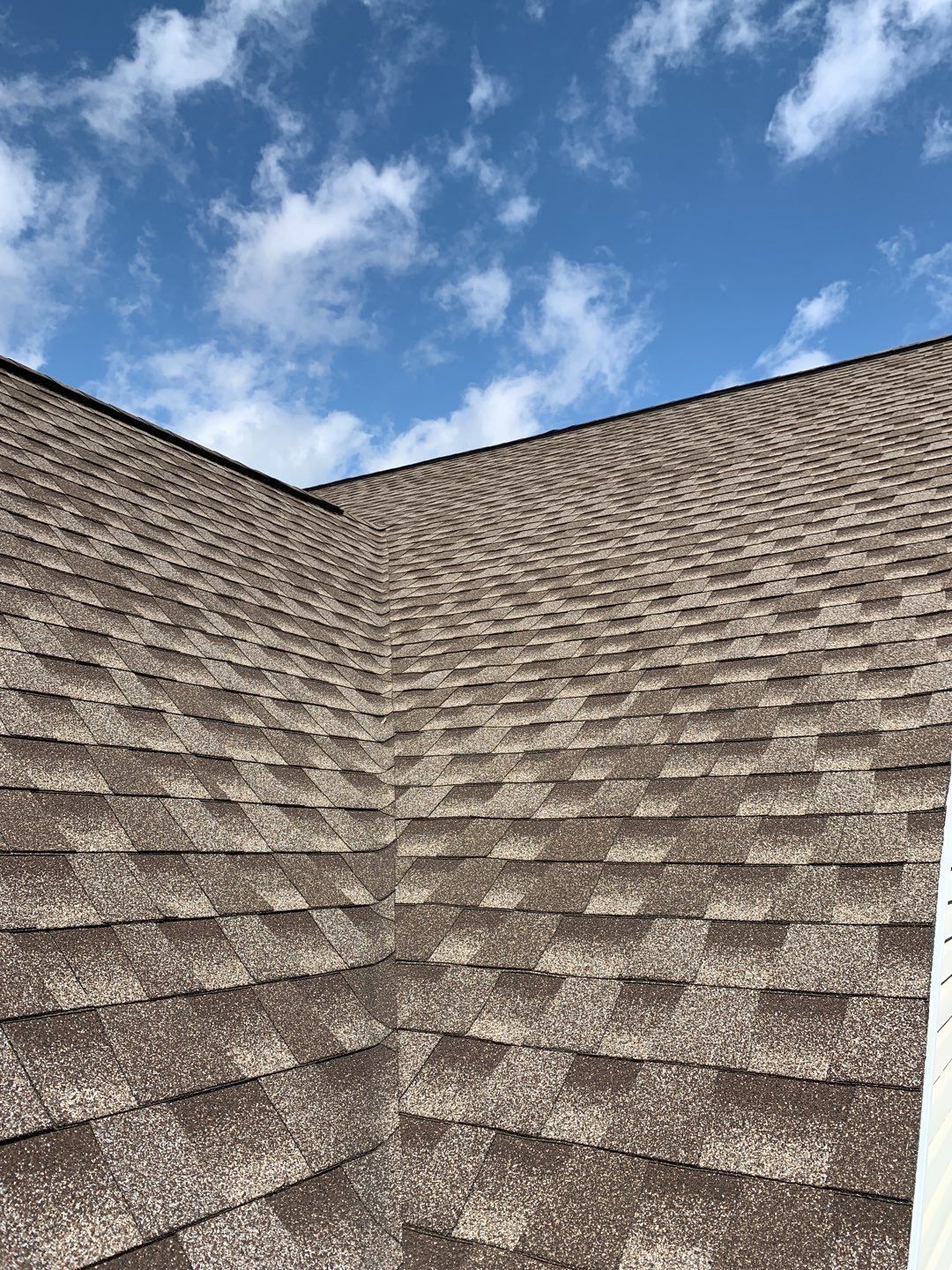Close-up of brown shingle roof slopes meeting under a blue sky with clouds