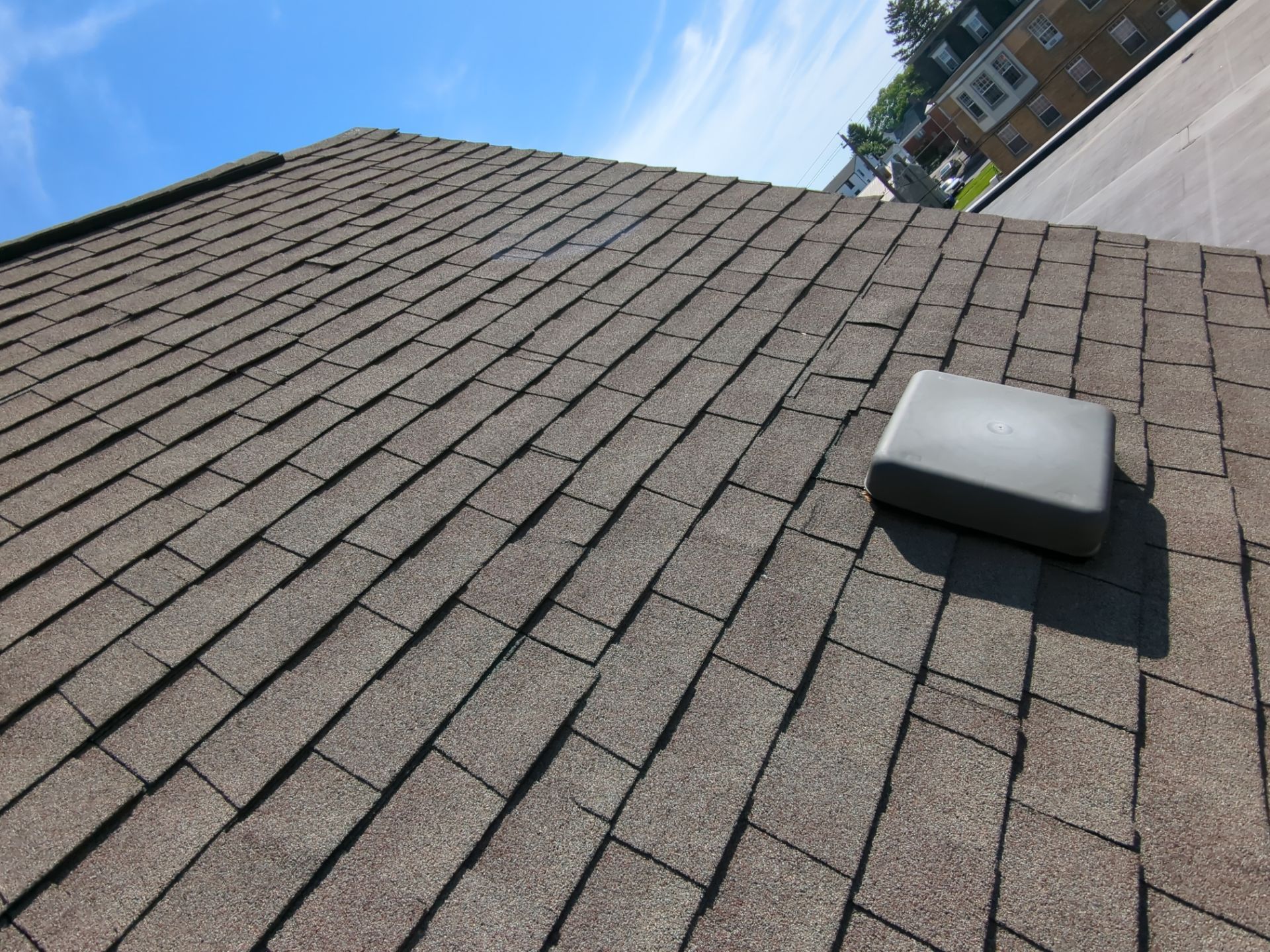 Angled view of a shingled roof with a small white vent under a blue sky