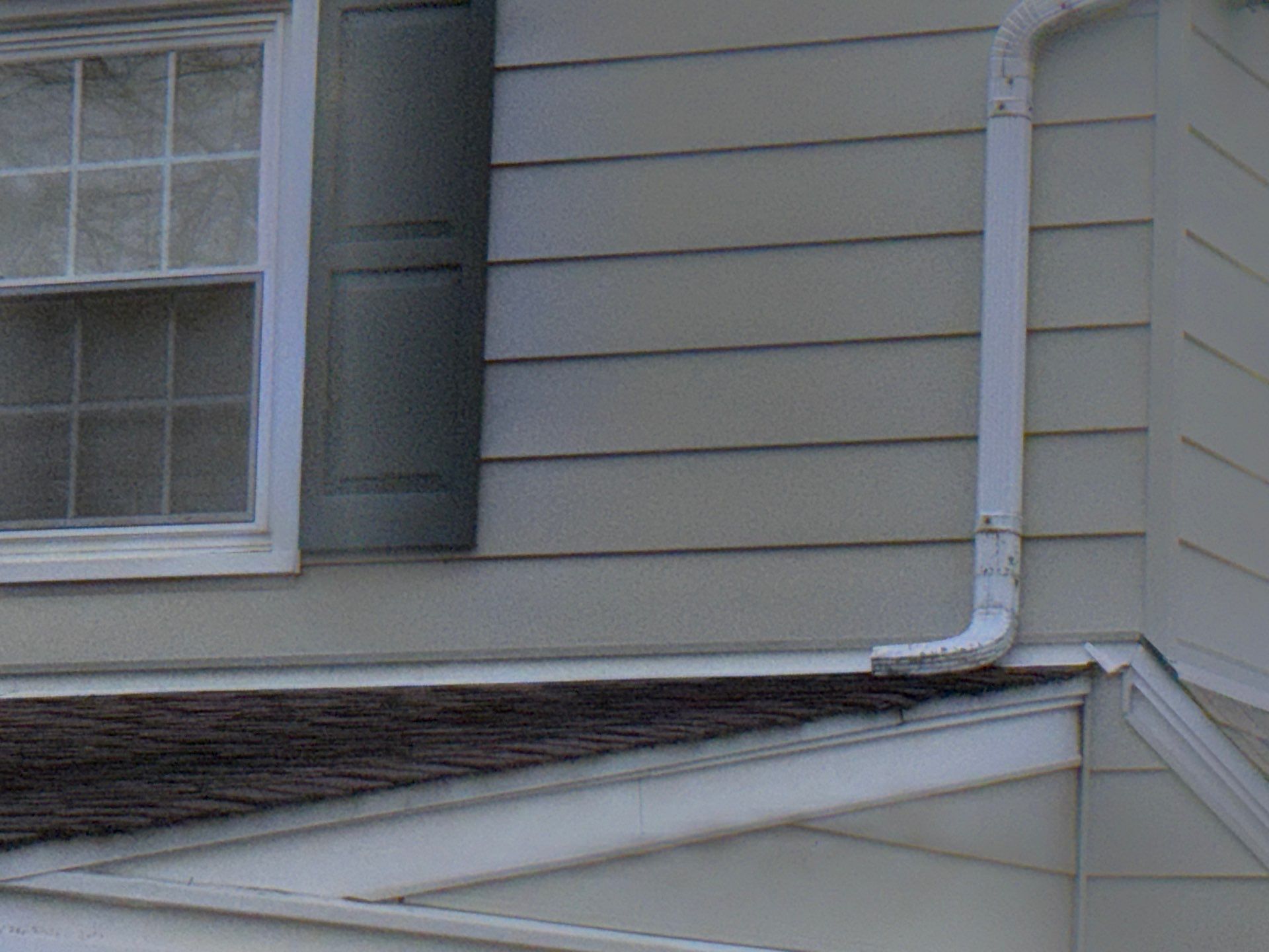 Roof-to-wall transition with weathered asphalt shingles, siding, and downspout on School Lane in Springfield PA
