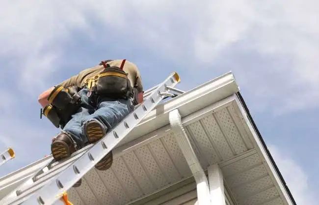 A person wearing dark pants and light-colored sneakers stands on the top platform of an aluminum step ladder.