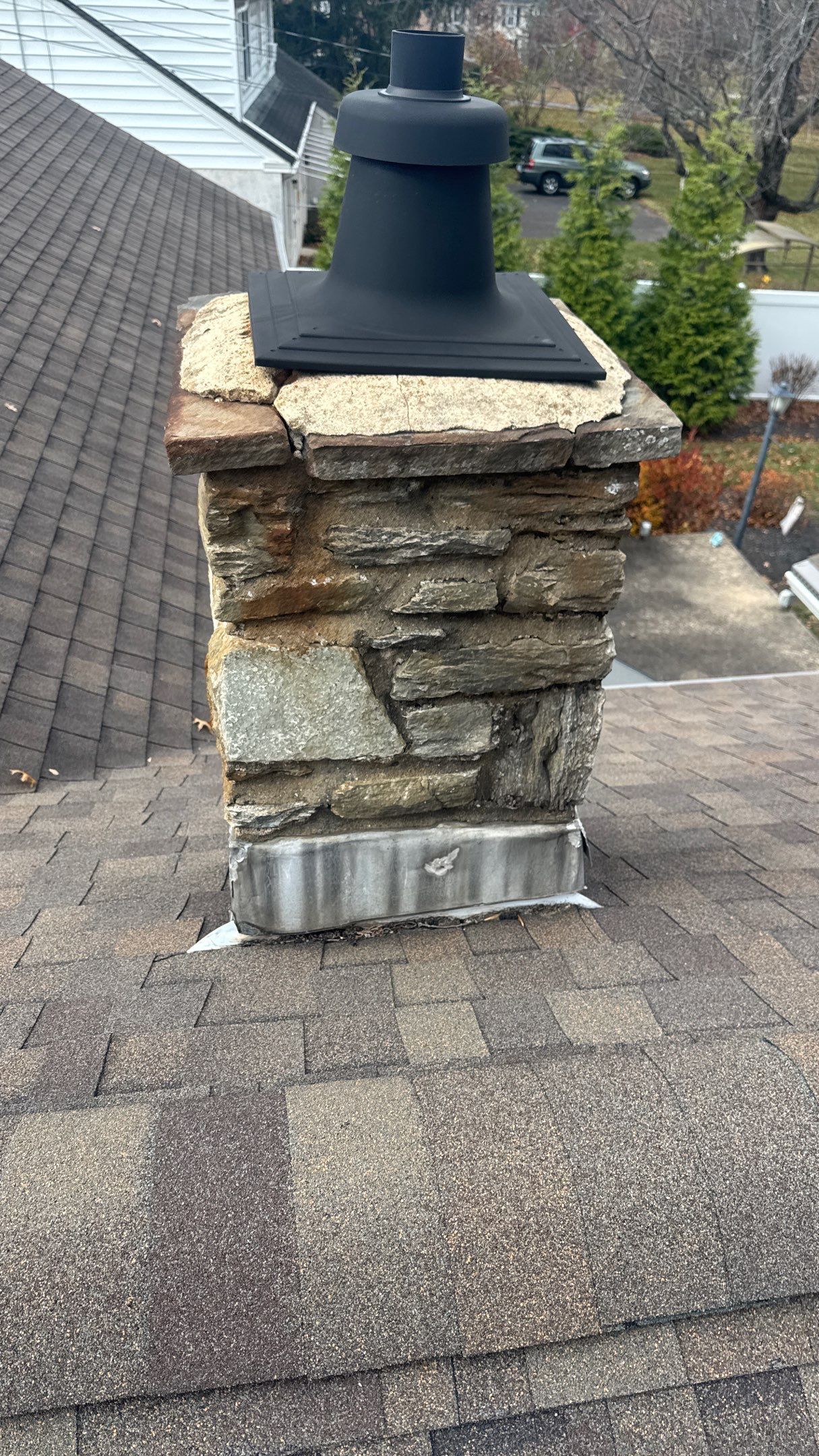 Roofing project on Oak Drive in Lansdale, PA showing an asphalt shingle roof, stone chimney, chimney cap, and metal flashing around the chimney base