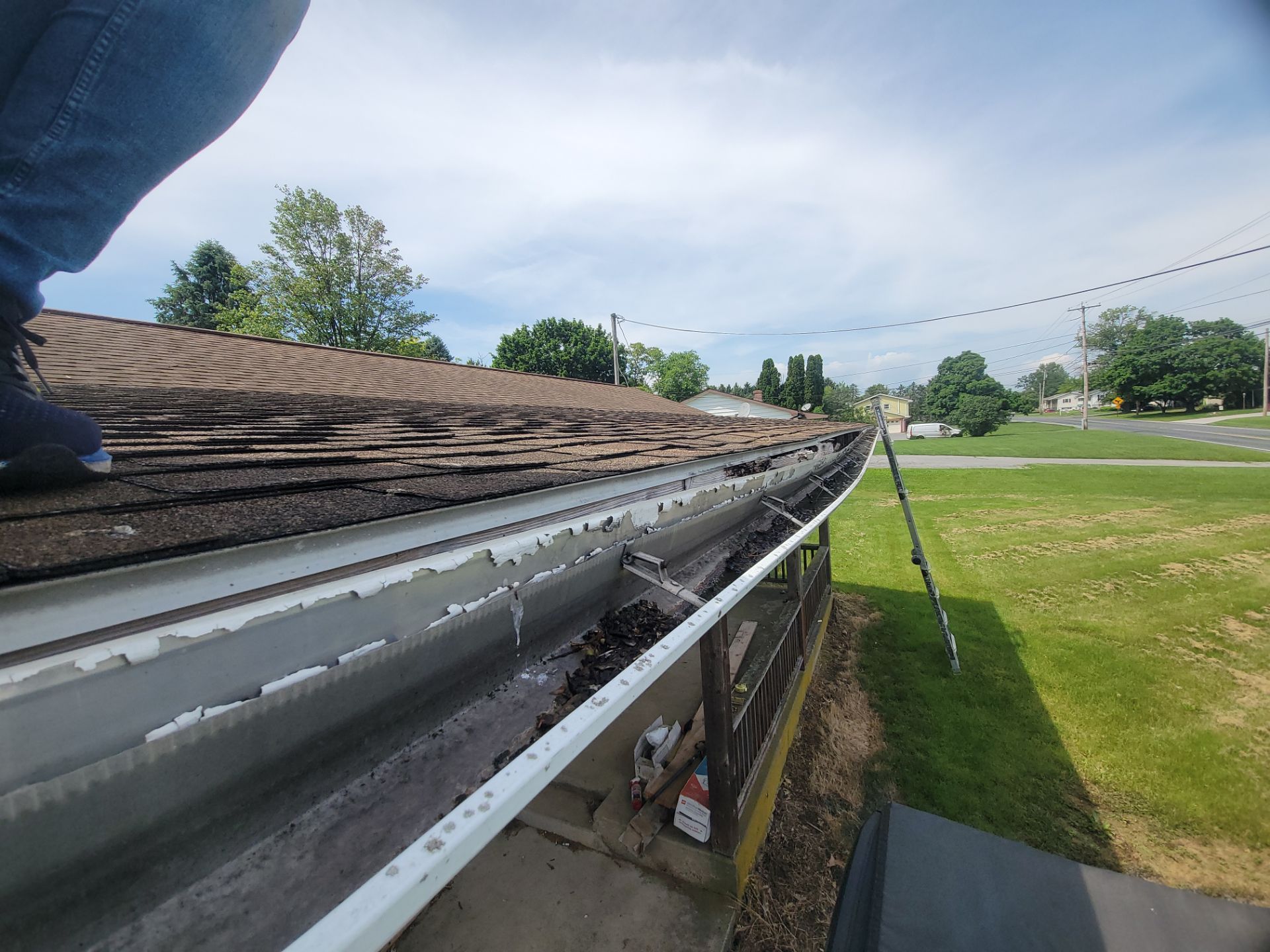 Close-up of a roof gutter being repaired beside a grassy field under a partly cloudy sky