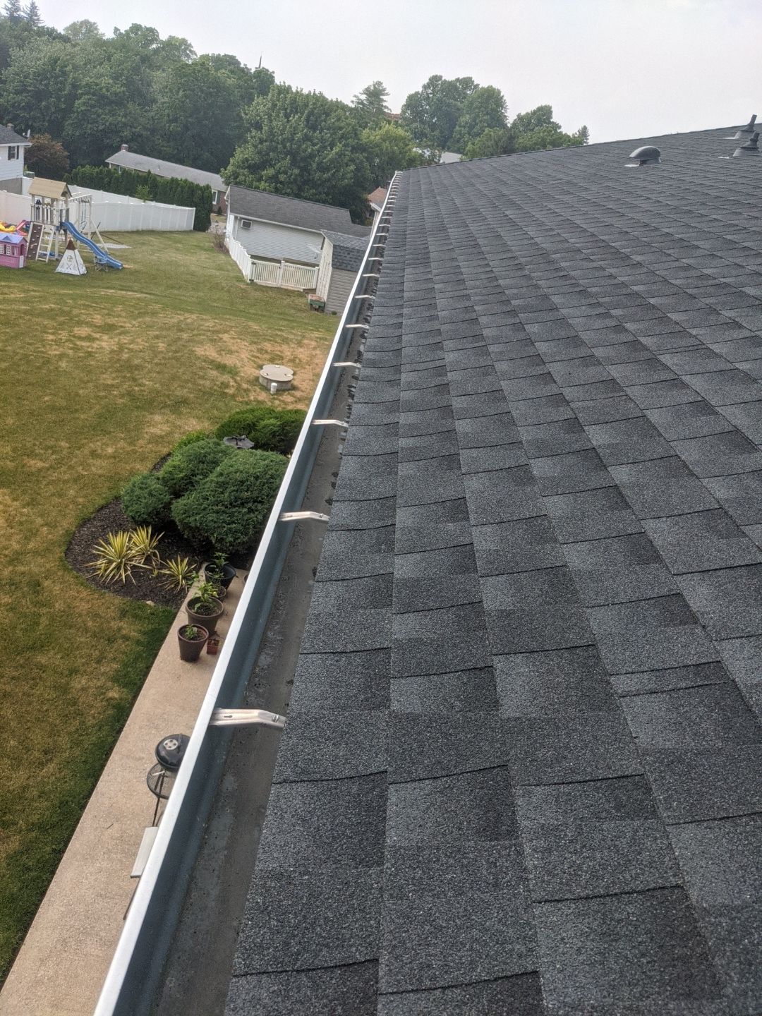 Roof shingles beside a grassy yard and white fence, viewed from above