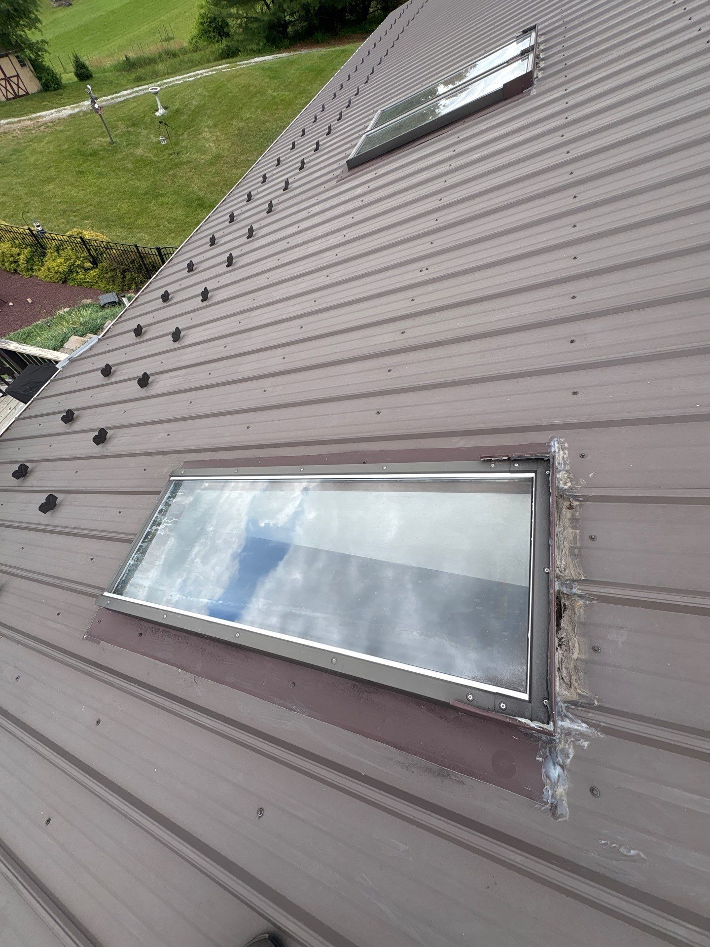 Sloped brown metal roof with two skylights, viewed from above.