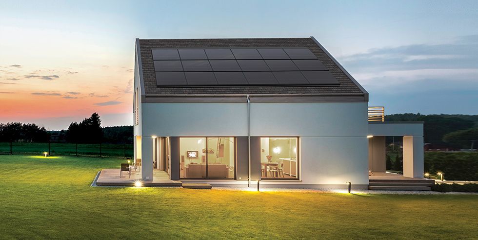 Modern house with solar panels on a green lawn at dusk, with ambient lighting.