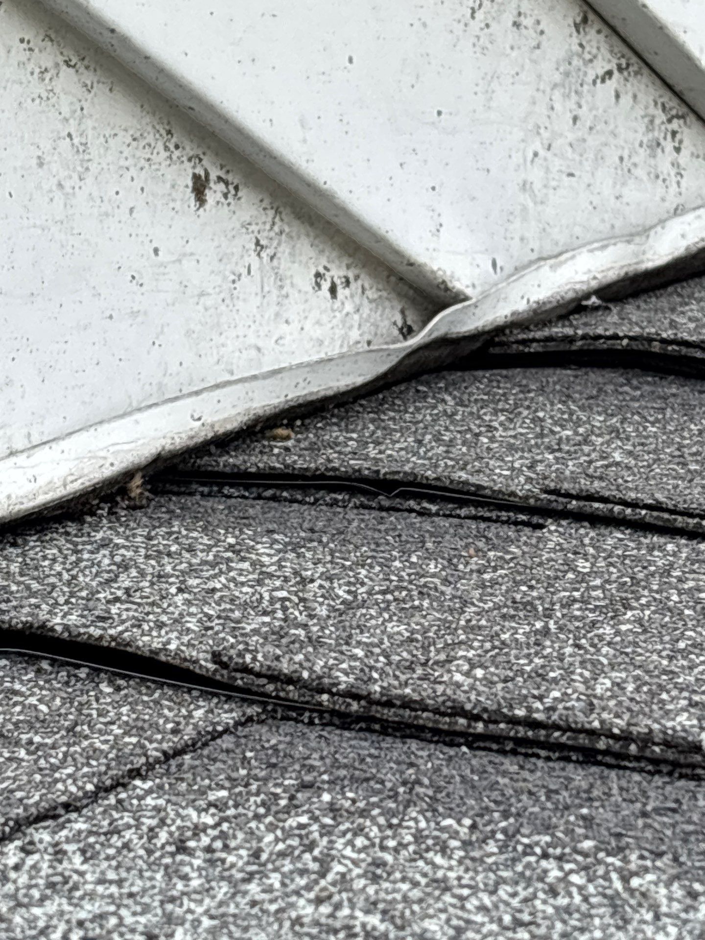 Lifted step flashing and loose asphalt shingles requiring roof repair on South Manheim Street.