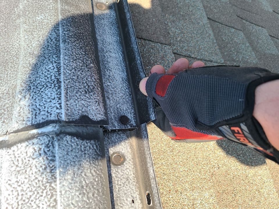 Gloved hand using a tool to scrape sealant from a roof shingle seam near a metal flashing edge