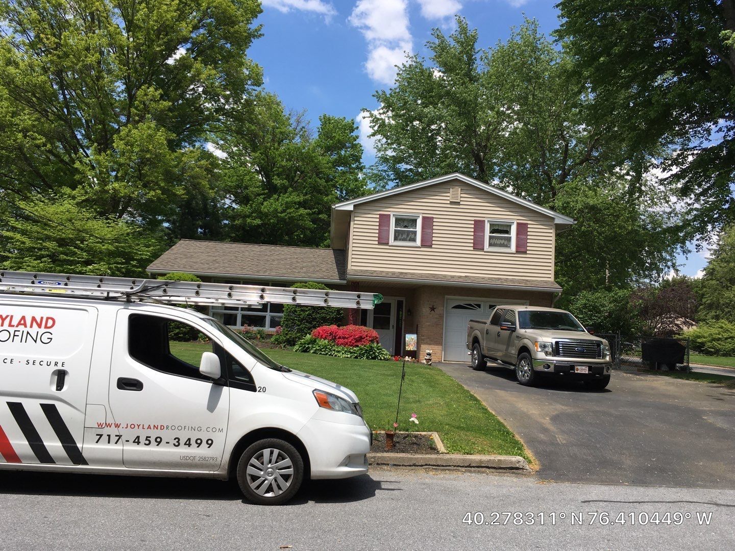 Suburban house with a driveway, parked SUV and van, surrounded by trees and flower beds.