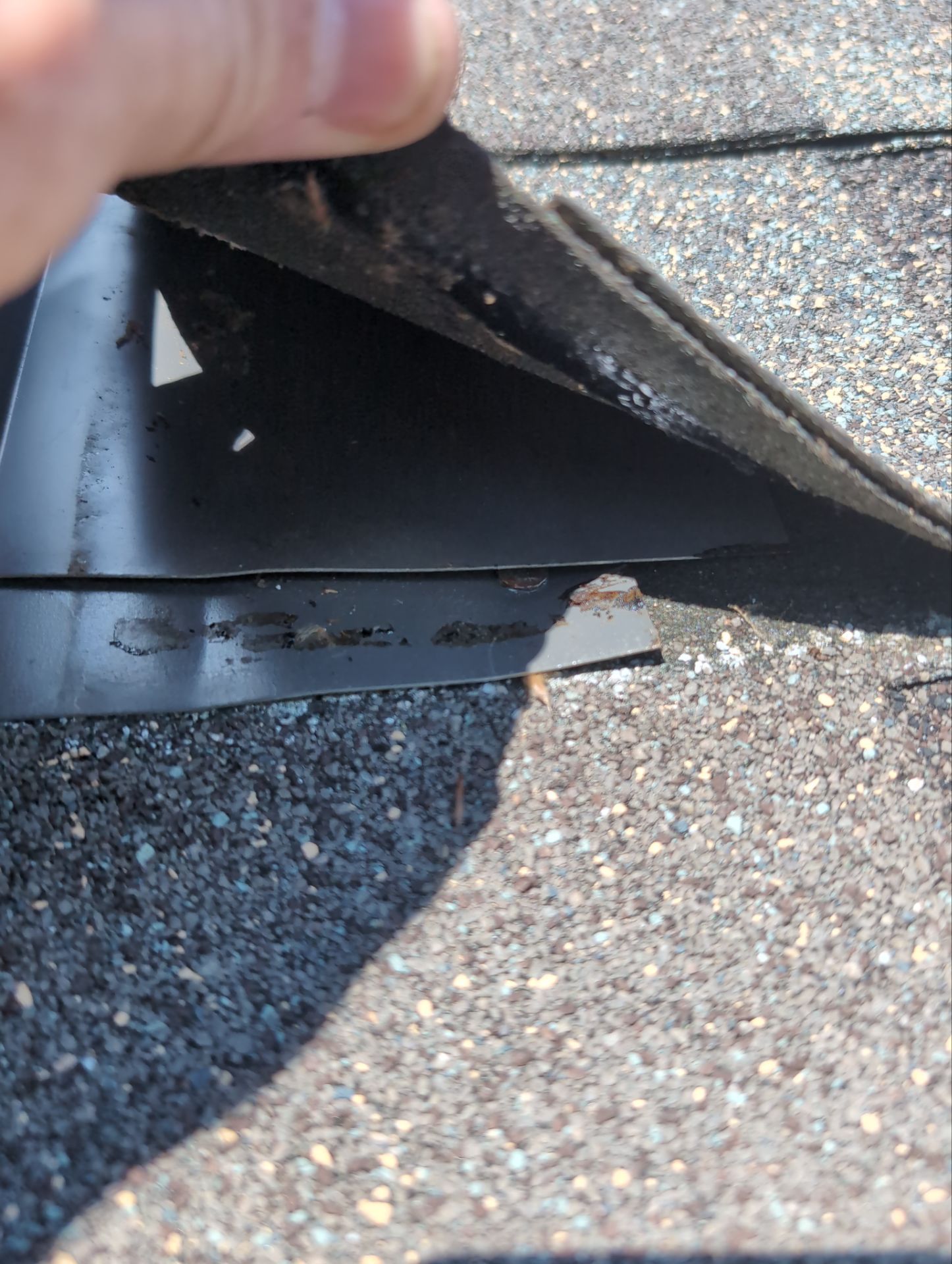 Hand lifting a torn black rubber mat on asphalt, revealing damaged material underneath