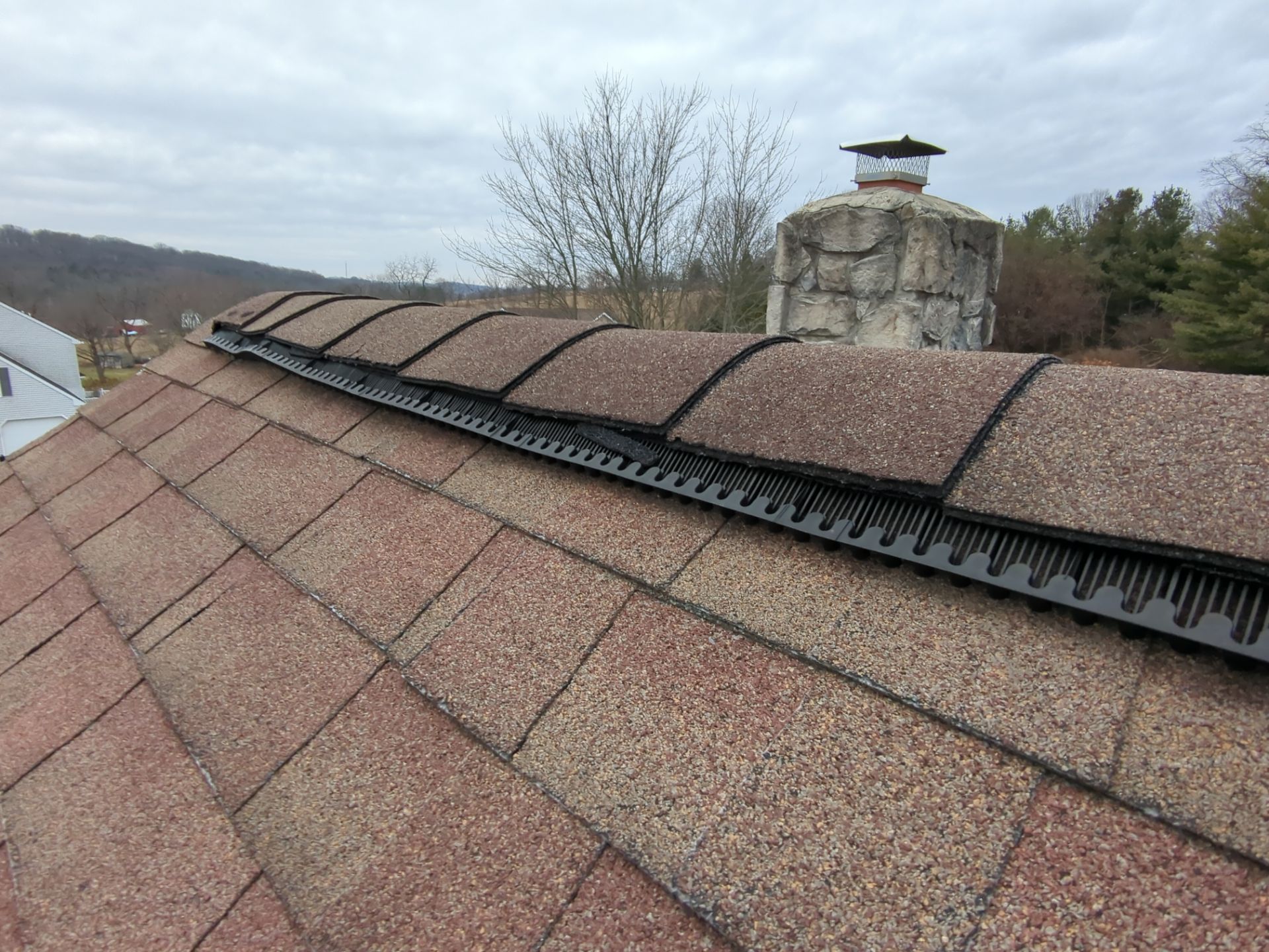 Ridge vent installed along an asphalt shingle roof near a stone chimney on Valley Road in Hamburg, PA.