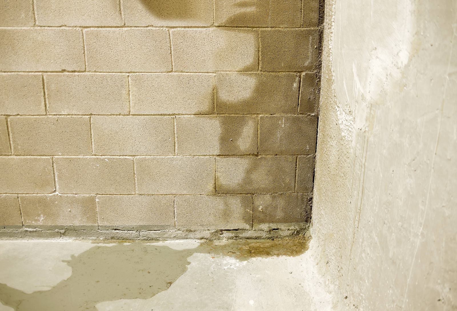 Damp cinder block wall meeting a white plaster wall with water stains on the floor