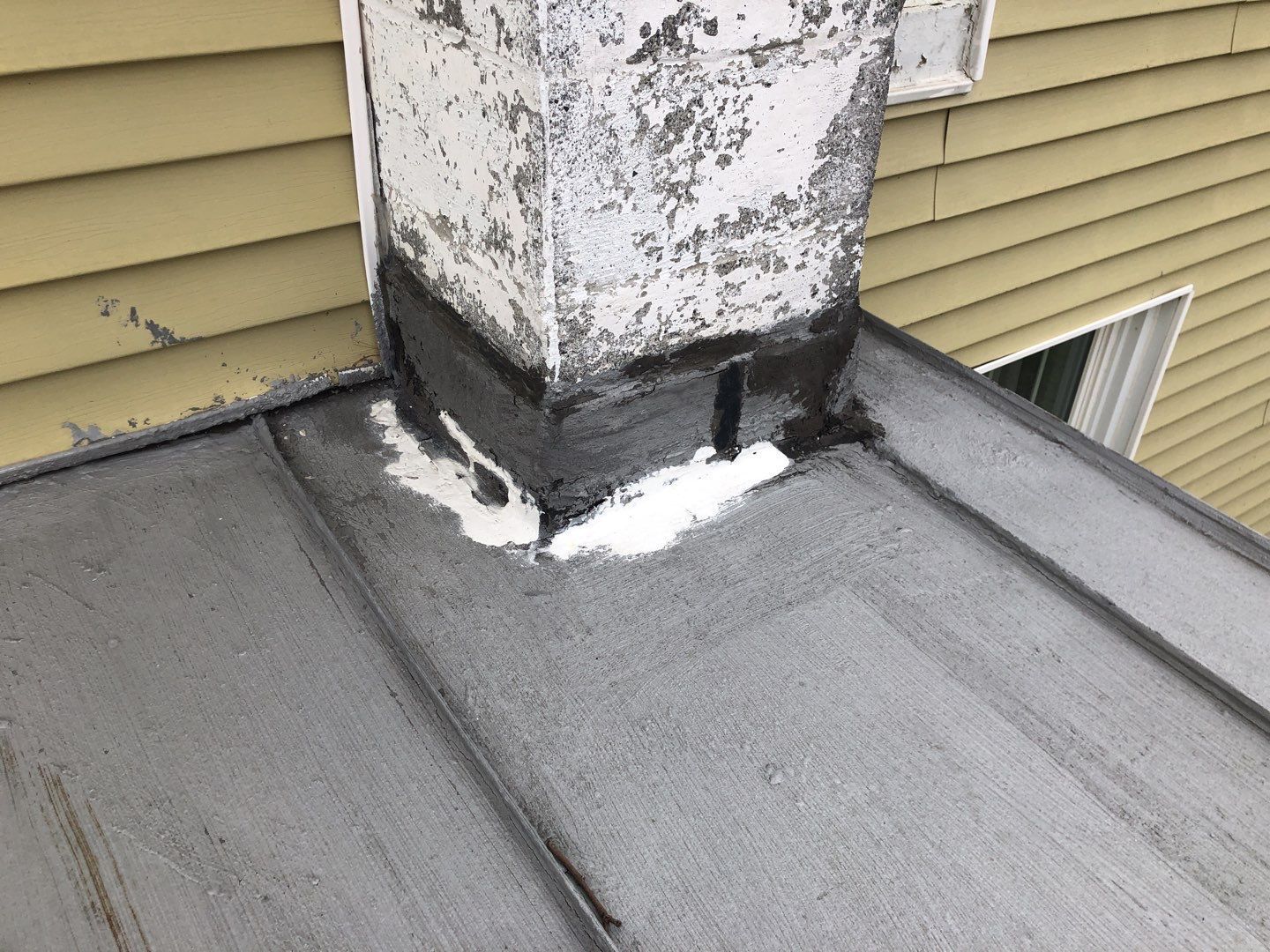 Close-up of a flat roof chimney with repaired flashing and sealant applied around the chimney base to address potential water intrusion.