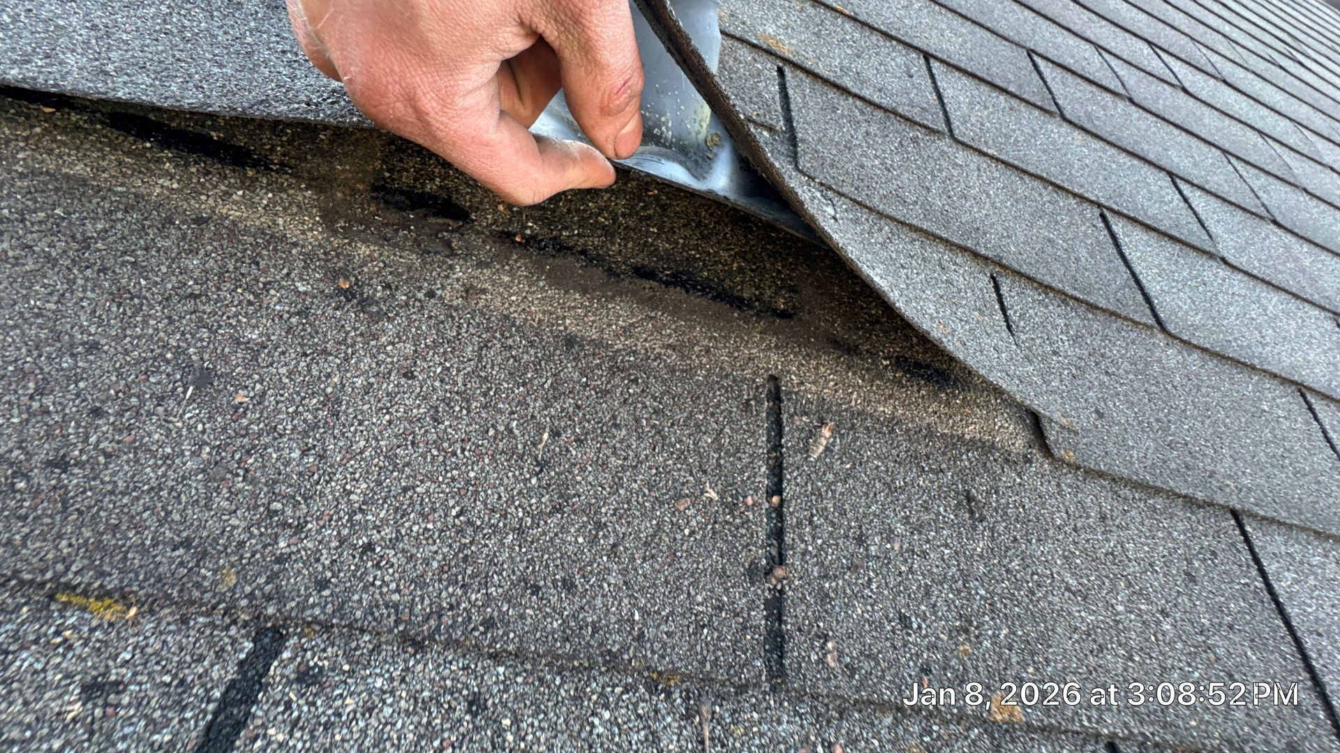 Damaged roof flashing lifted beneath asphalt shingles during a roof inspection on Windsor Way.