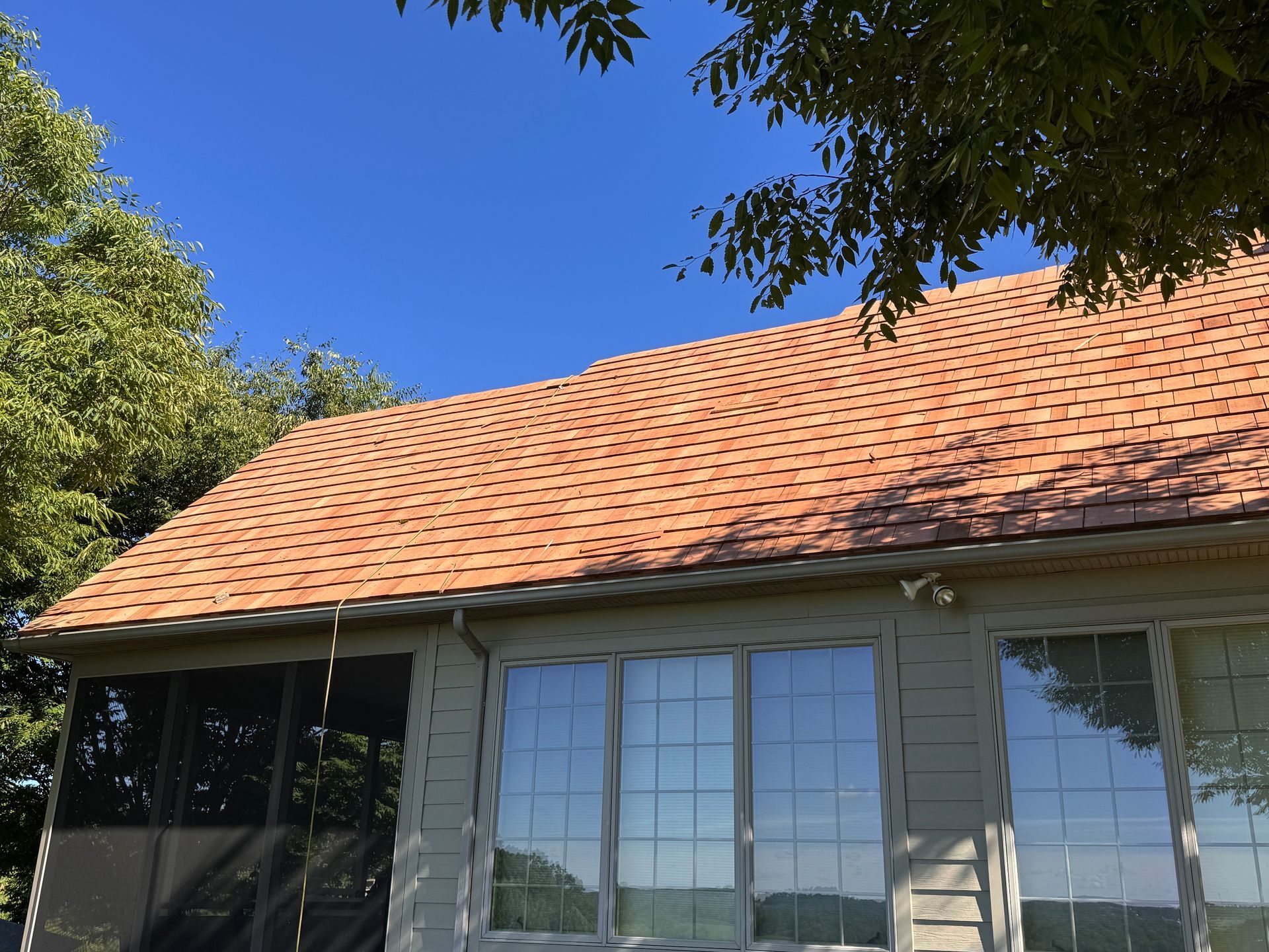 House with orange tile roof and windows under blue sky, framed by leafy trees