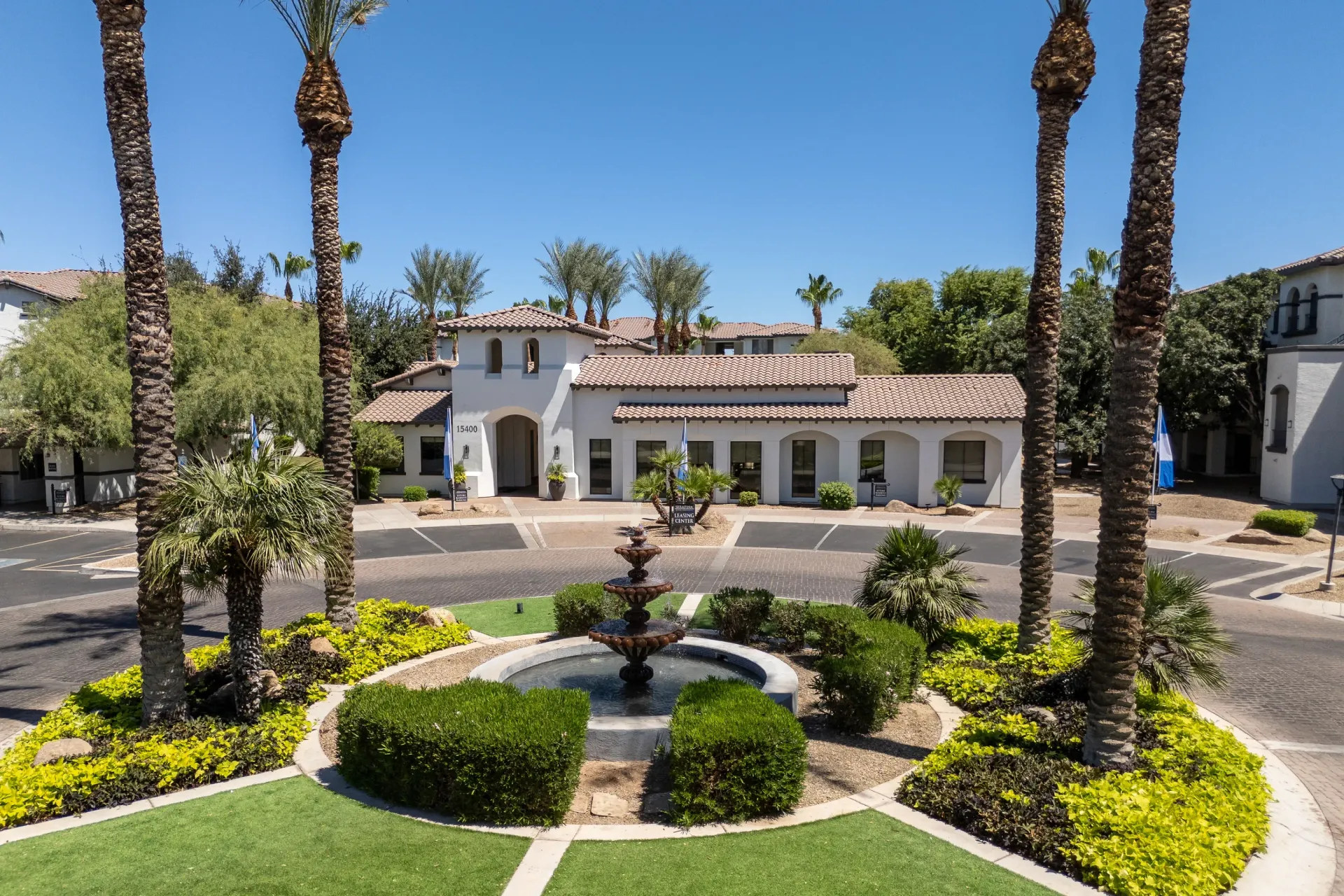 Community entrance with a fountain and palm trees.