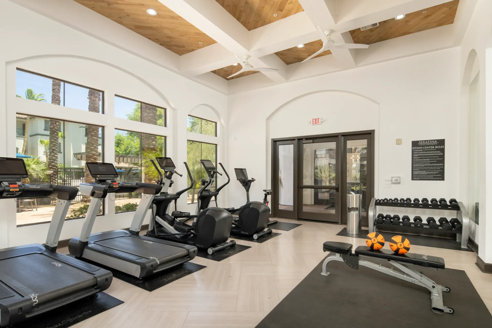 Fitness center with treadmills, elliptical machines, weight bench, and dumbbells.