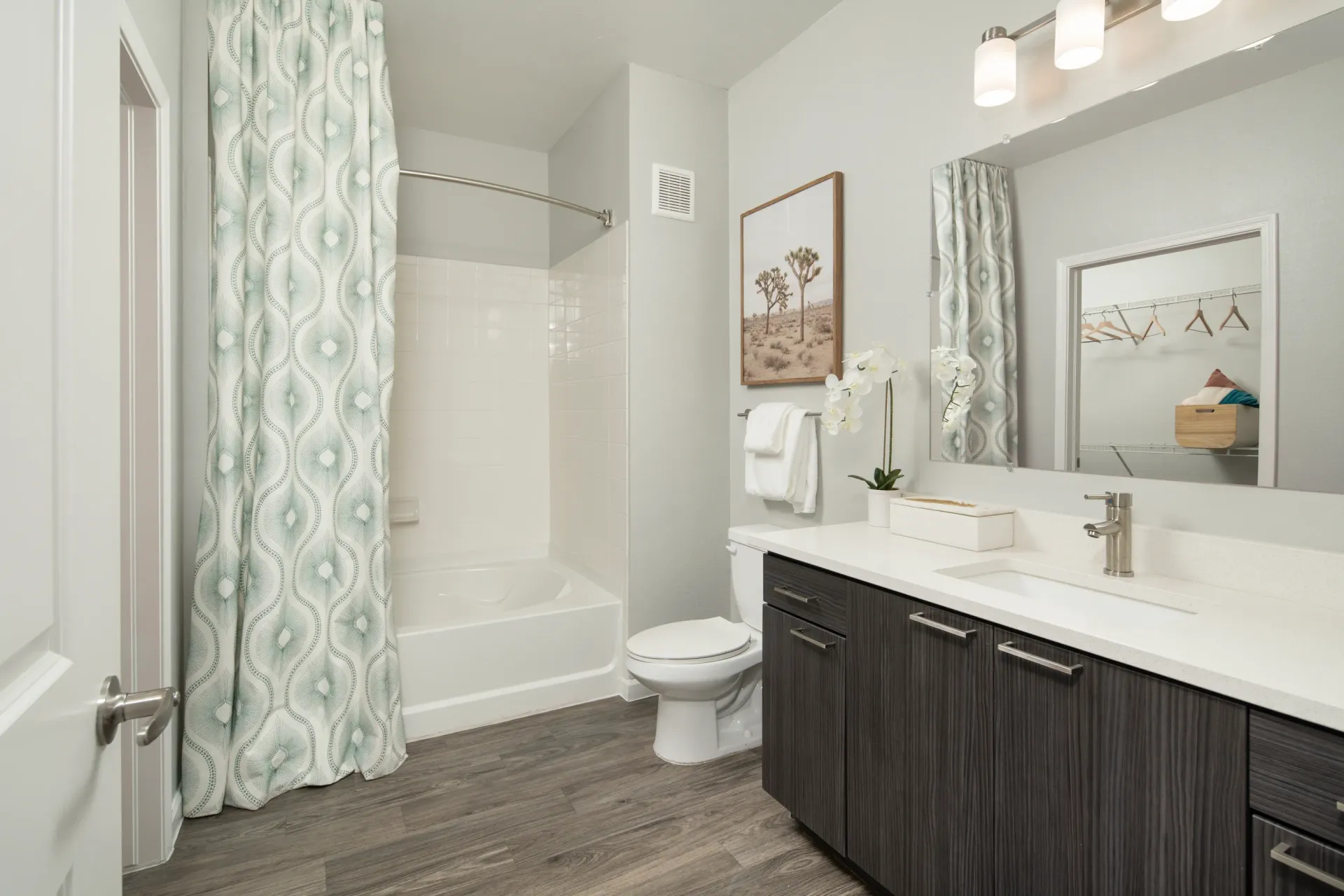 Modern bathroom with a soaking tub, toilet, and vanity with a large mirror and walk-in closet.