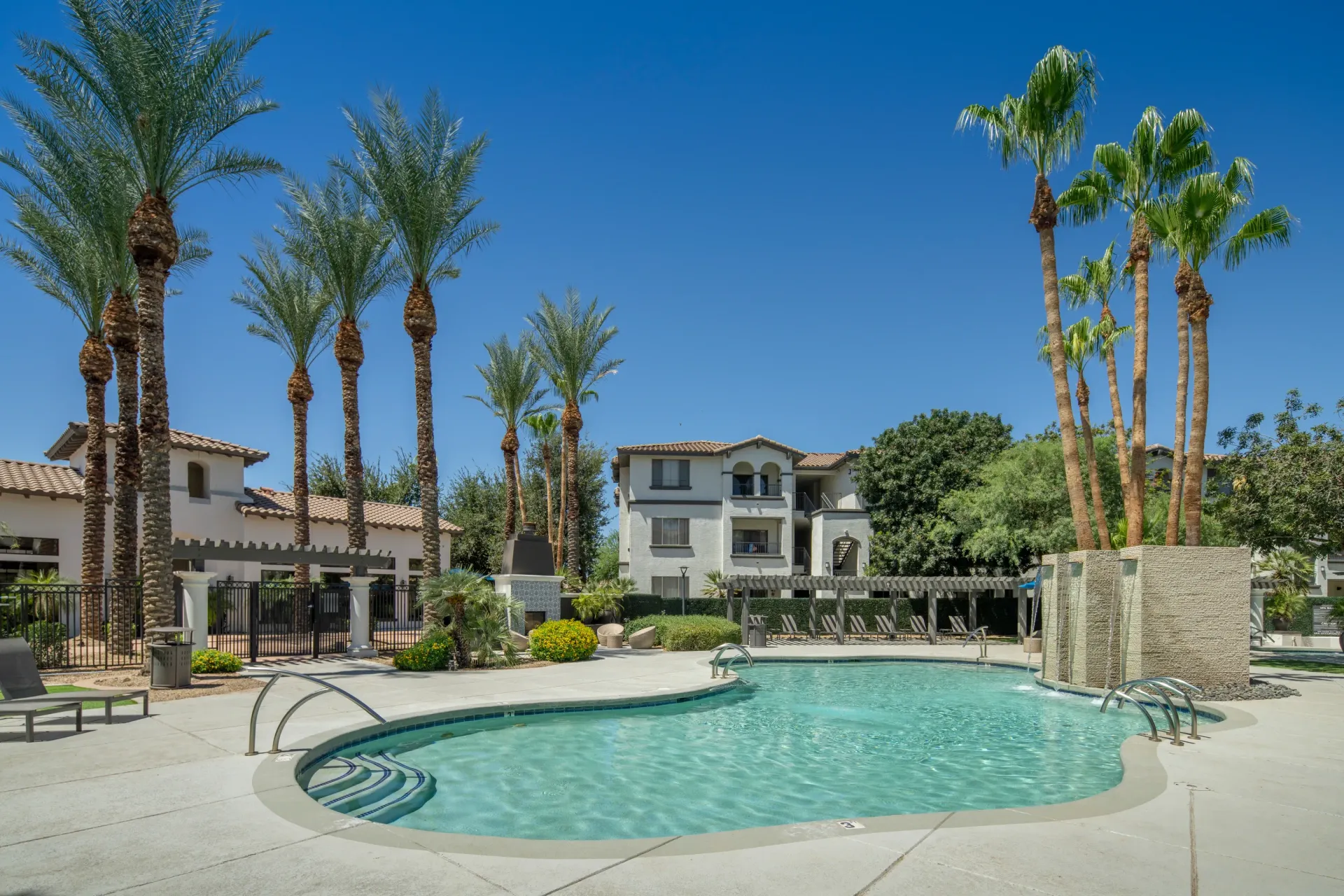 Luxury apartment complex swimming pool with palm trees and lounge chairs.
