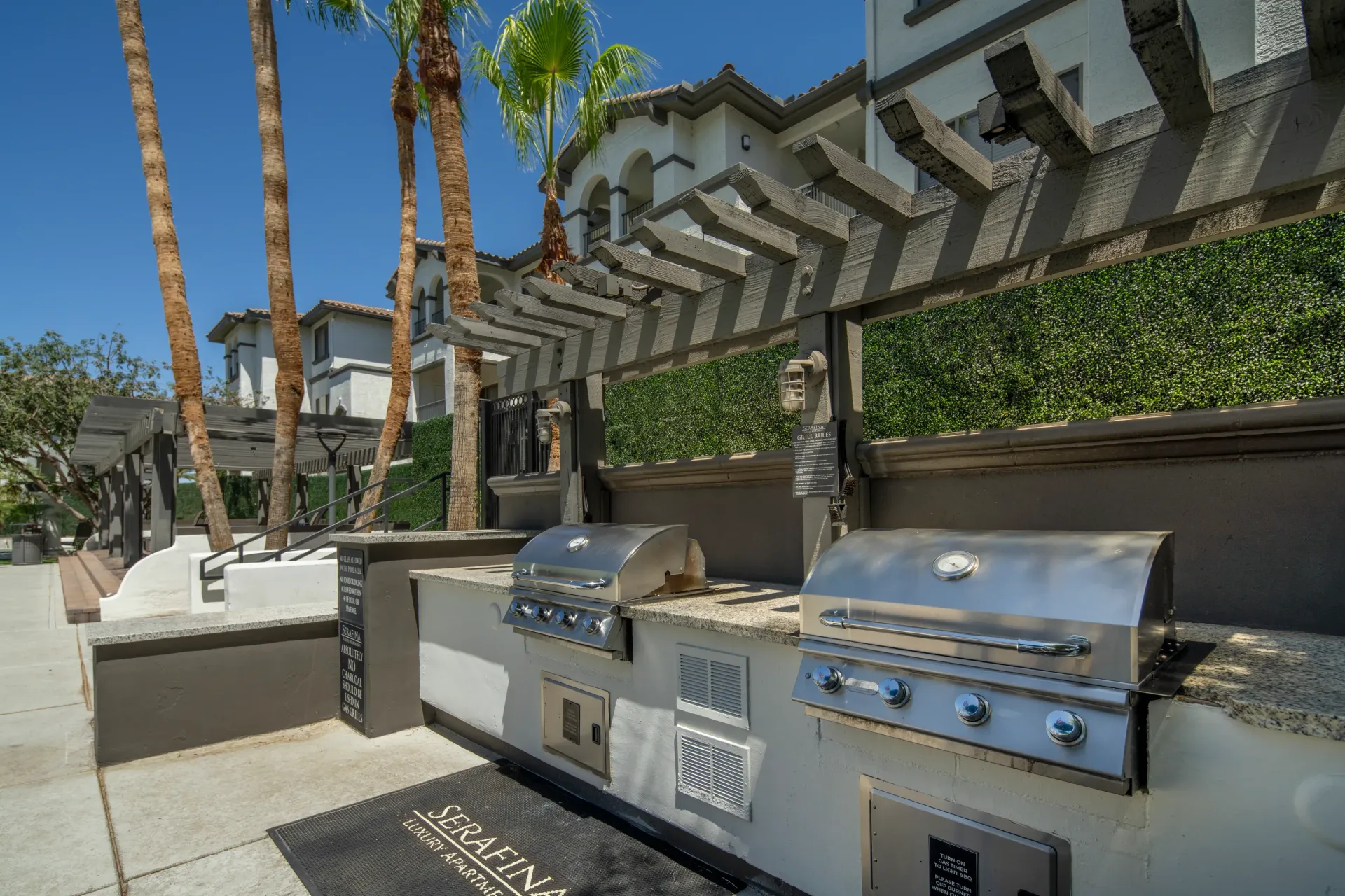 Outdoor grilling station with two stainless steel grills and palm trees.