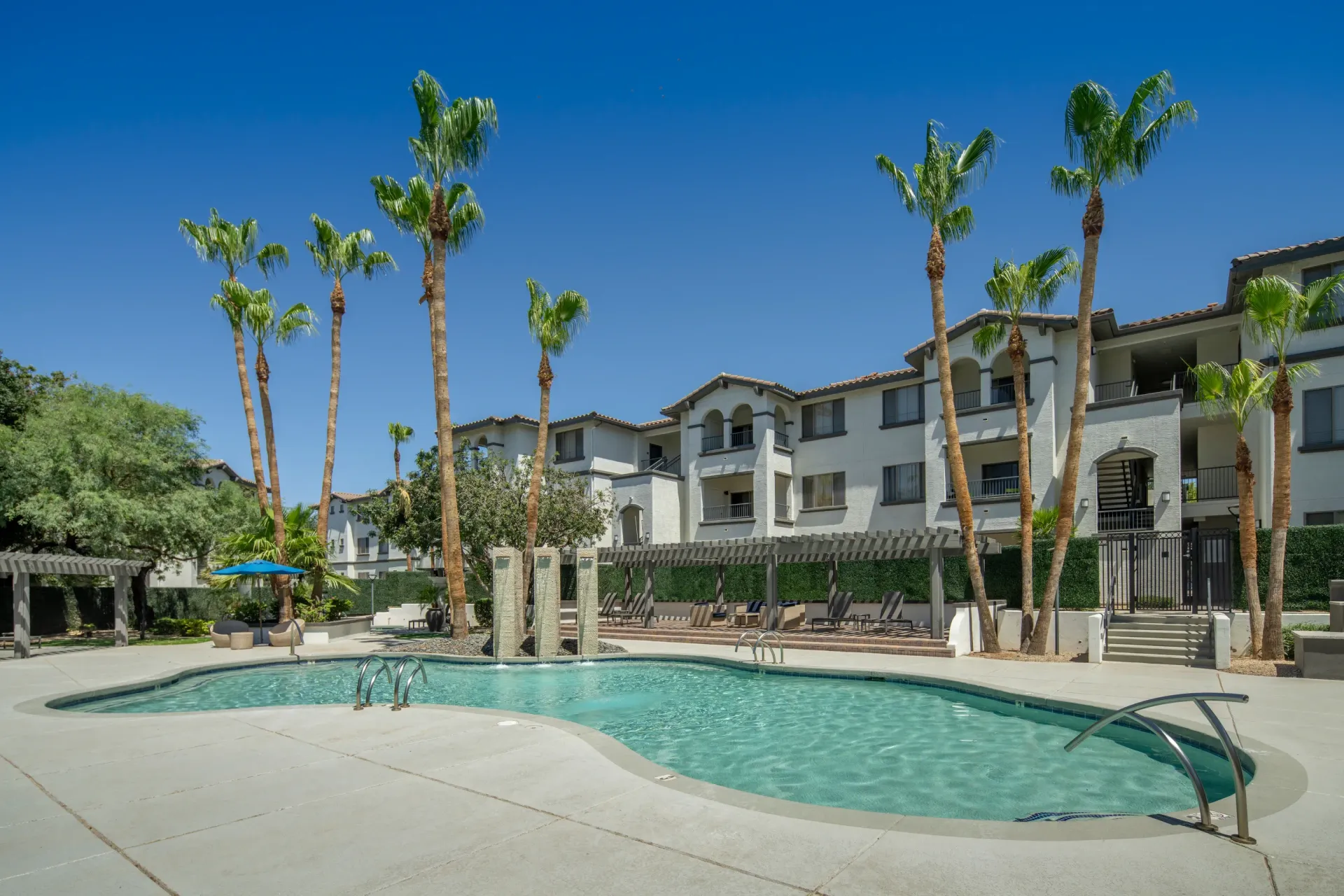Curving swimming pool with palm trees and apartment buildings in the background.