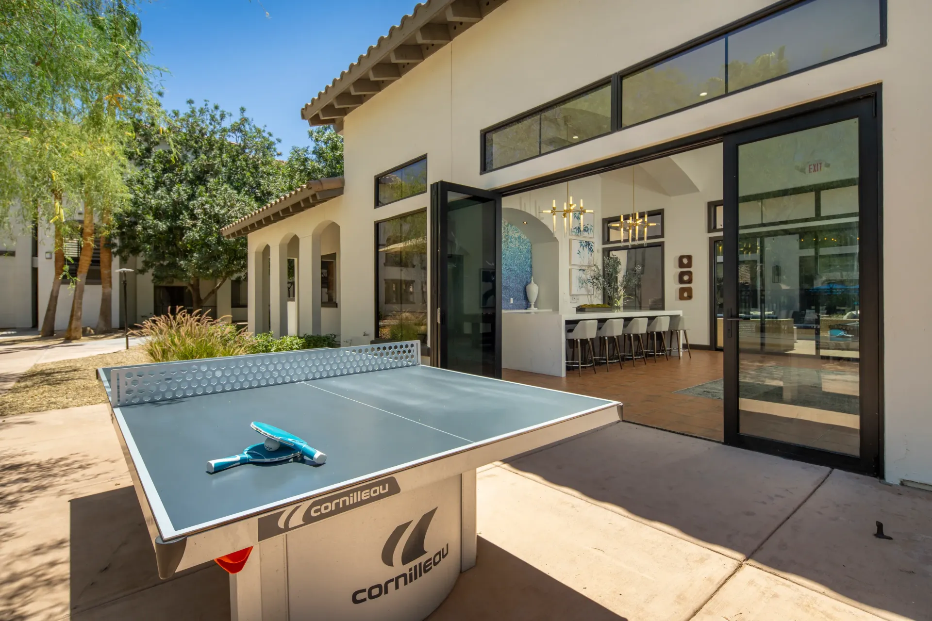 Ping pong table with paddles and ball outside a building with open doors revealing a bar area.