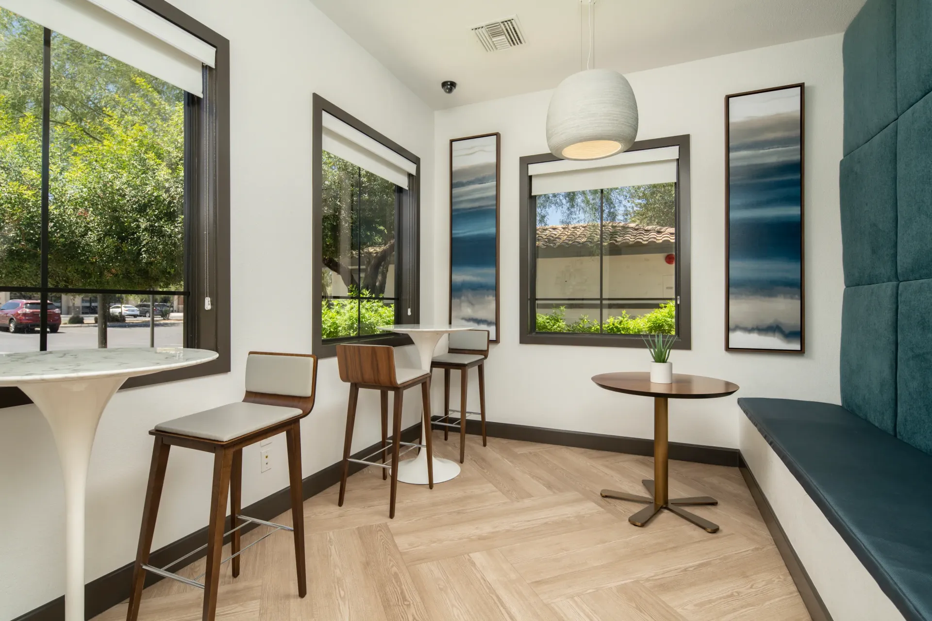 Modern community lounge area with bar stools and tables near large windows.