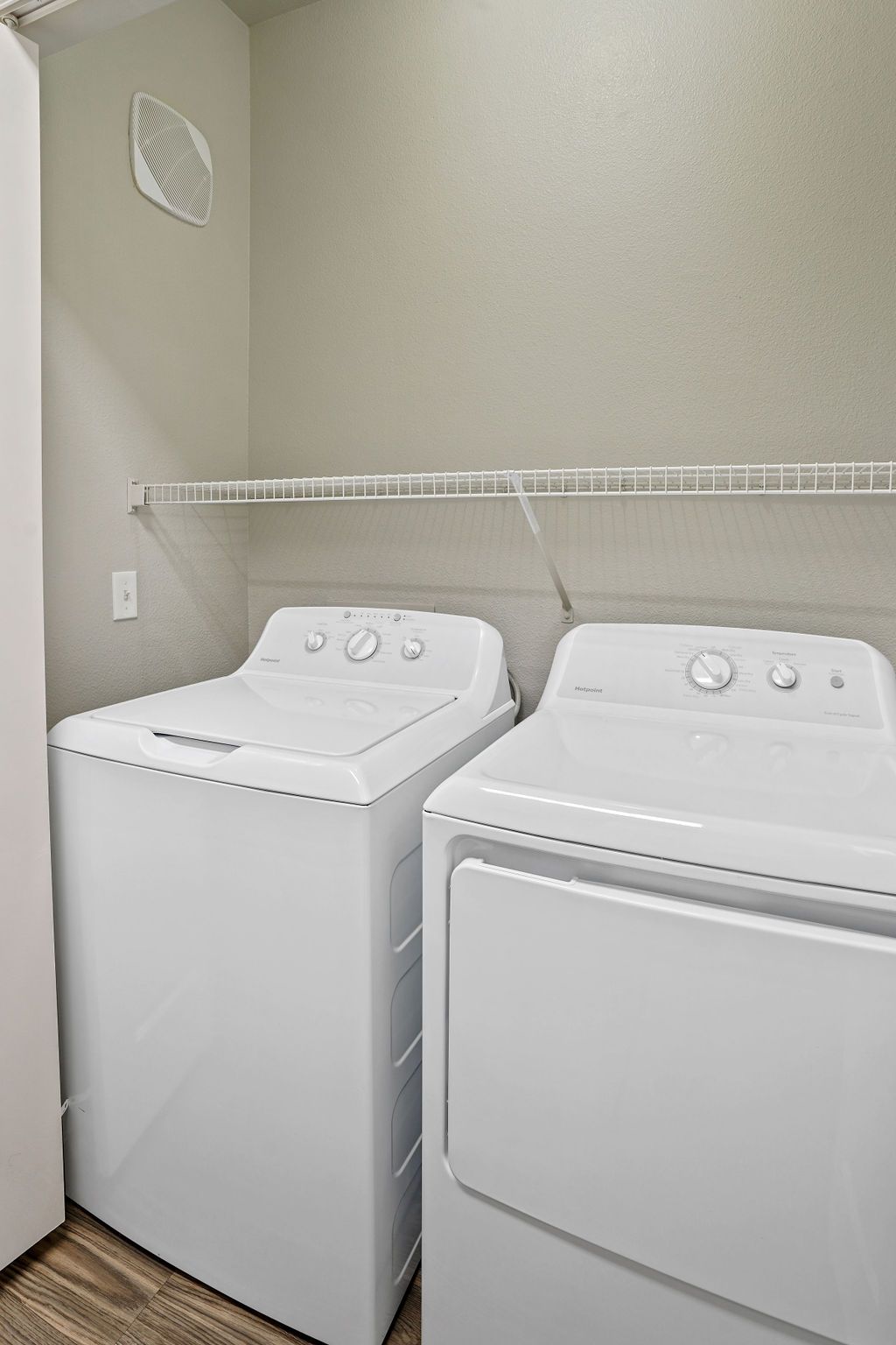Laundry room with two white machines (washer and dryer) side by side and a wire shelf above.
